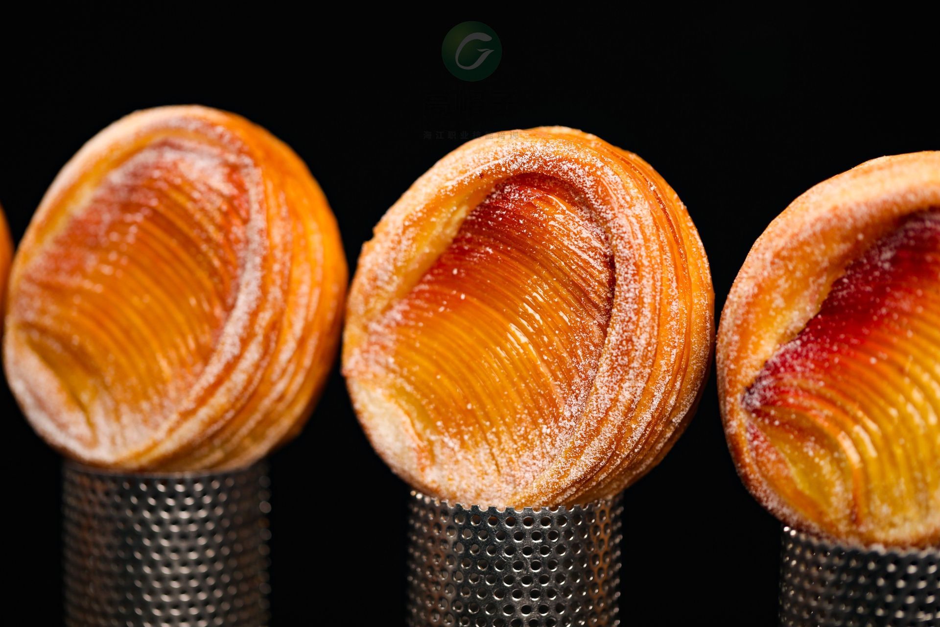 Une rangée de pâtisseries posées sur des récipients en métal sur fond noir.