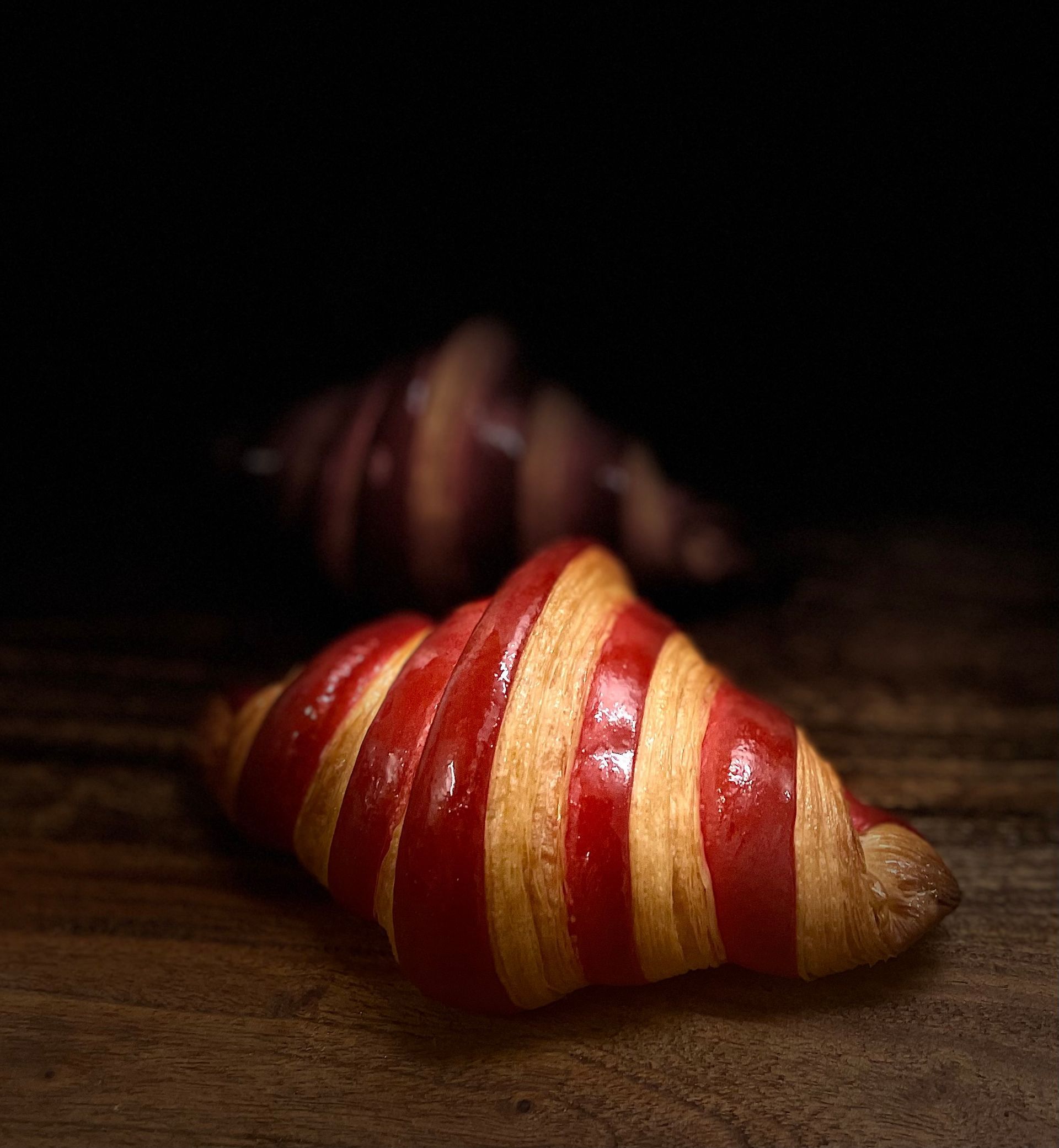 Un croissant rayé rouge et jaune est posé sur une table en bois.