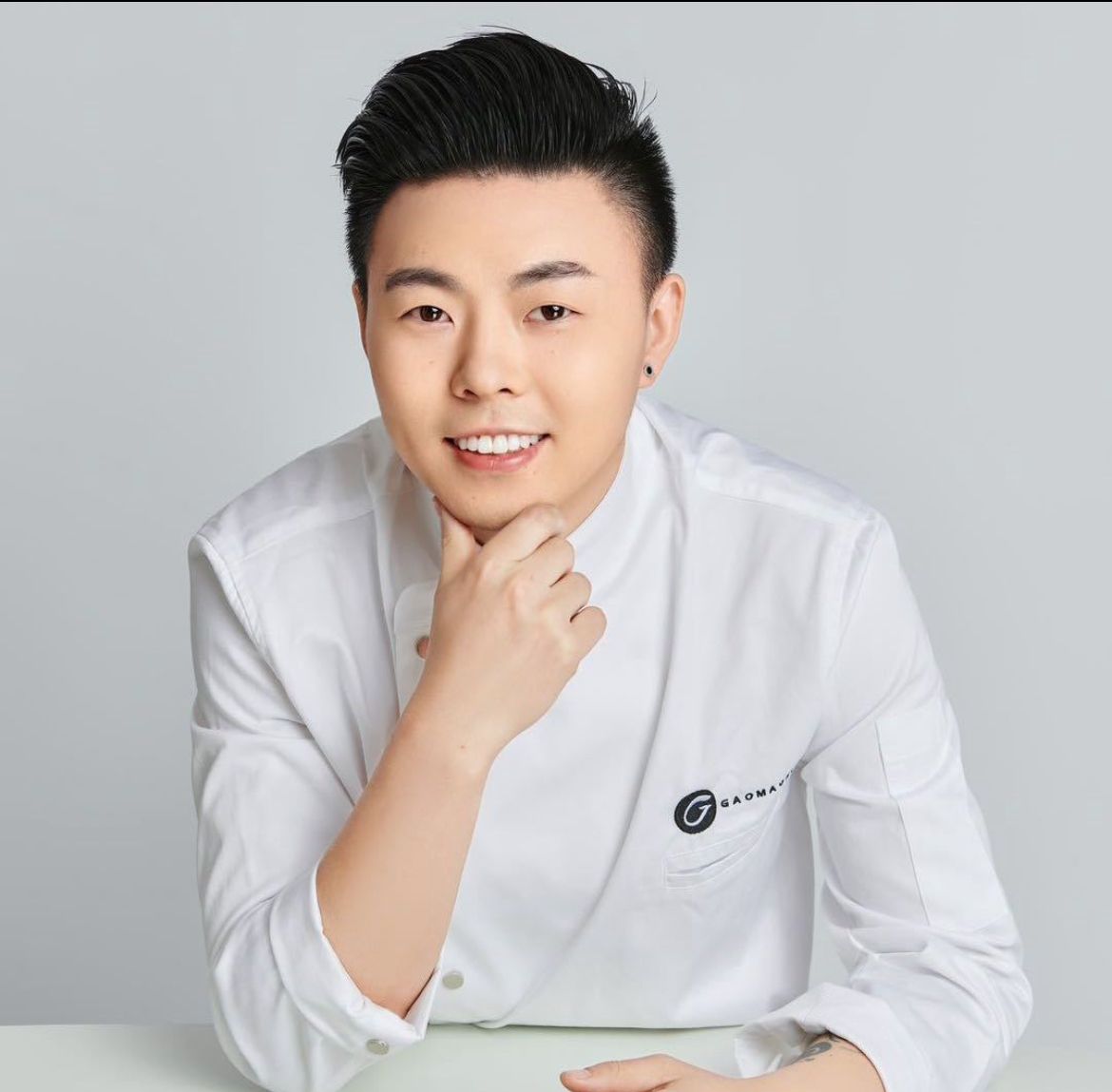 Un homme en chemise blanche est assis à une table avec sa main sur son menton.