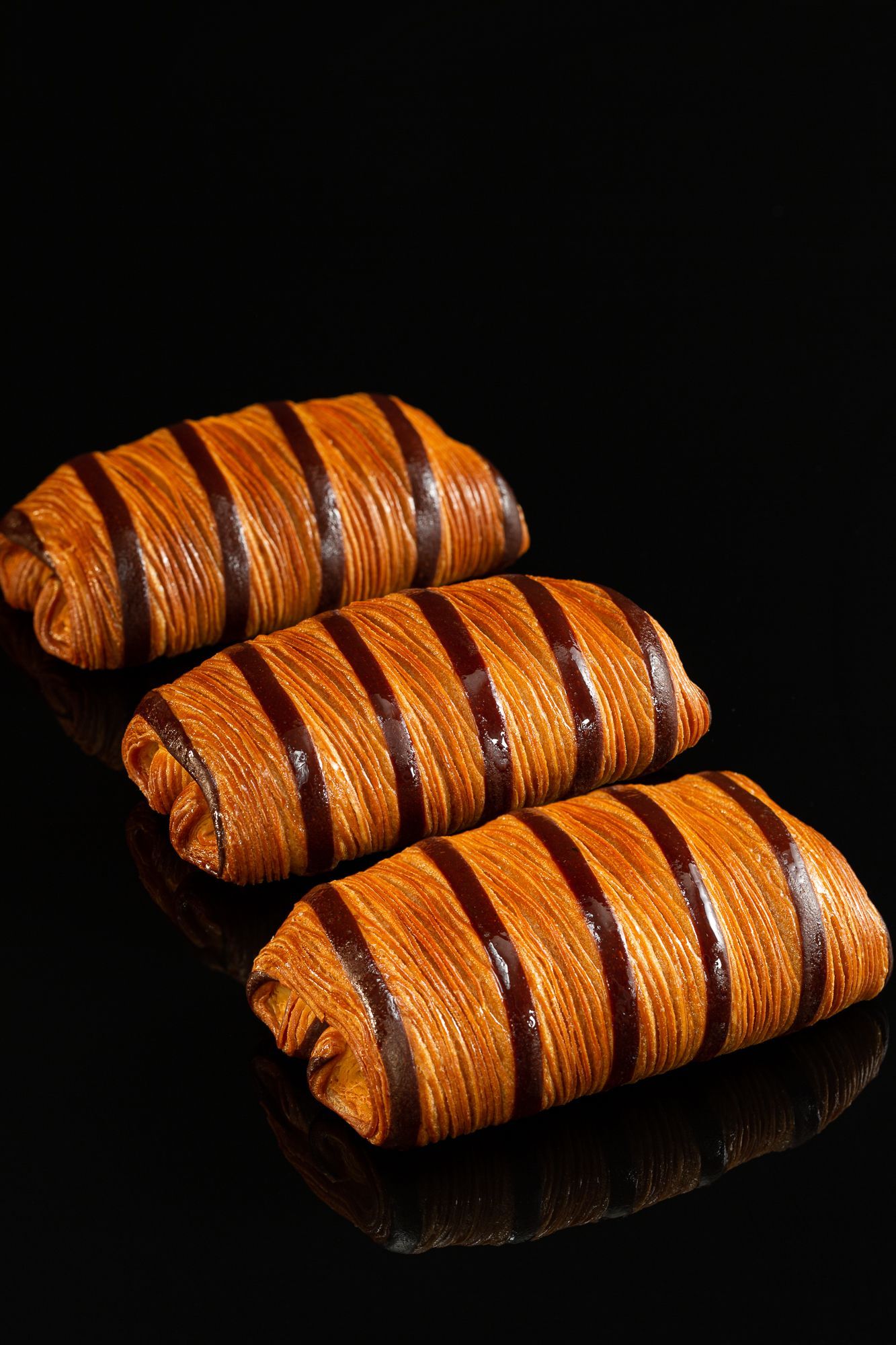 Trois croissants avec glaçage au chocolat sur une surface noire.