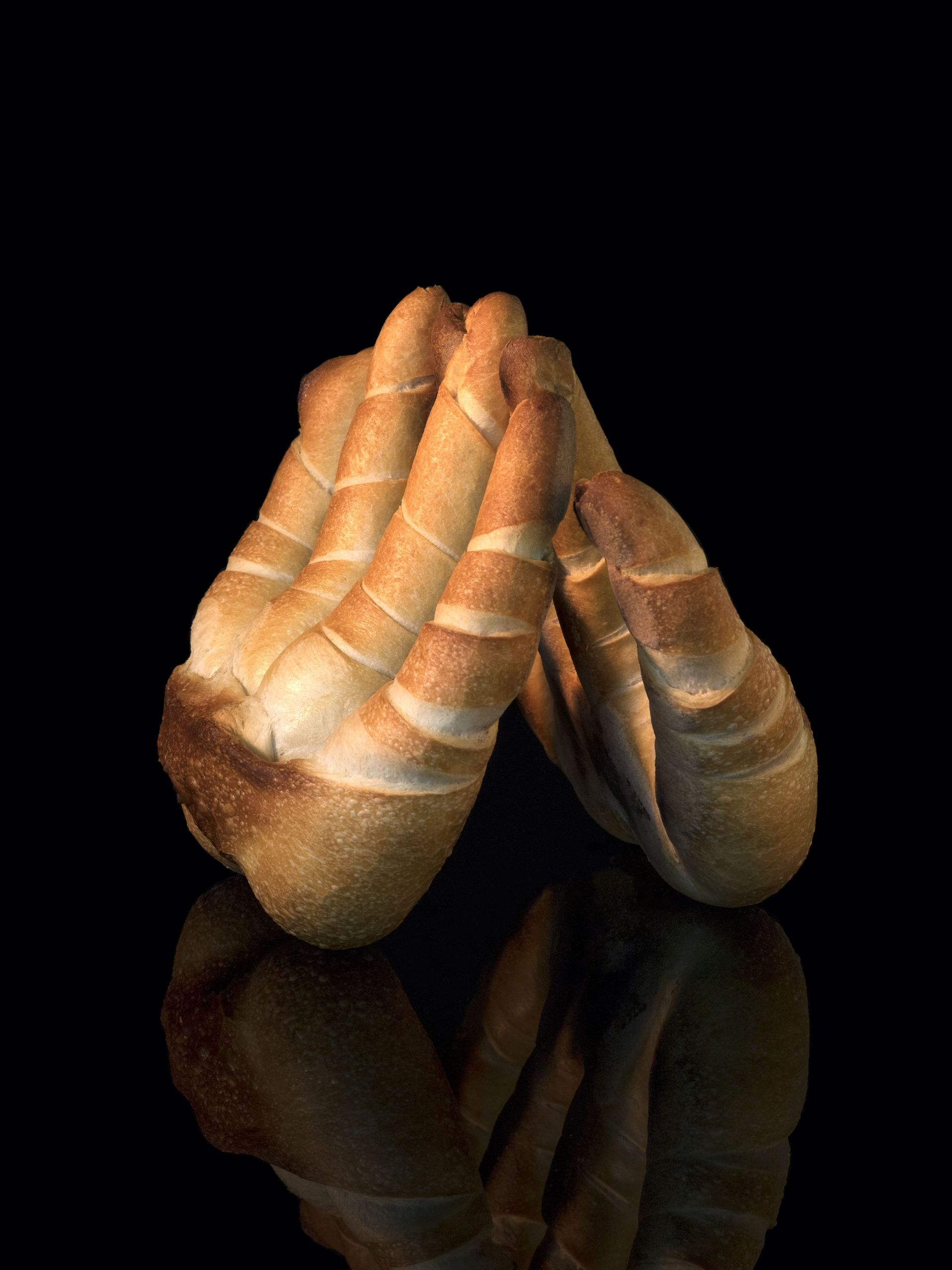 Une paire de mains en prière faites de pain sur une surface noire