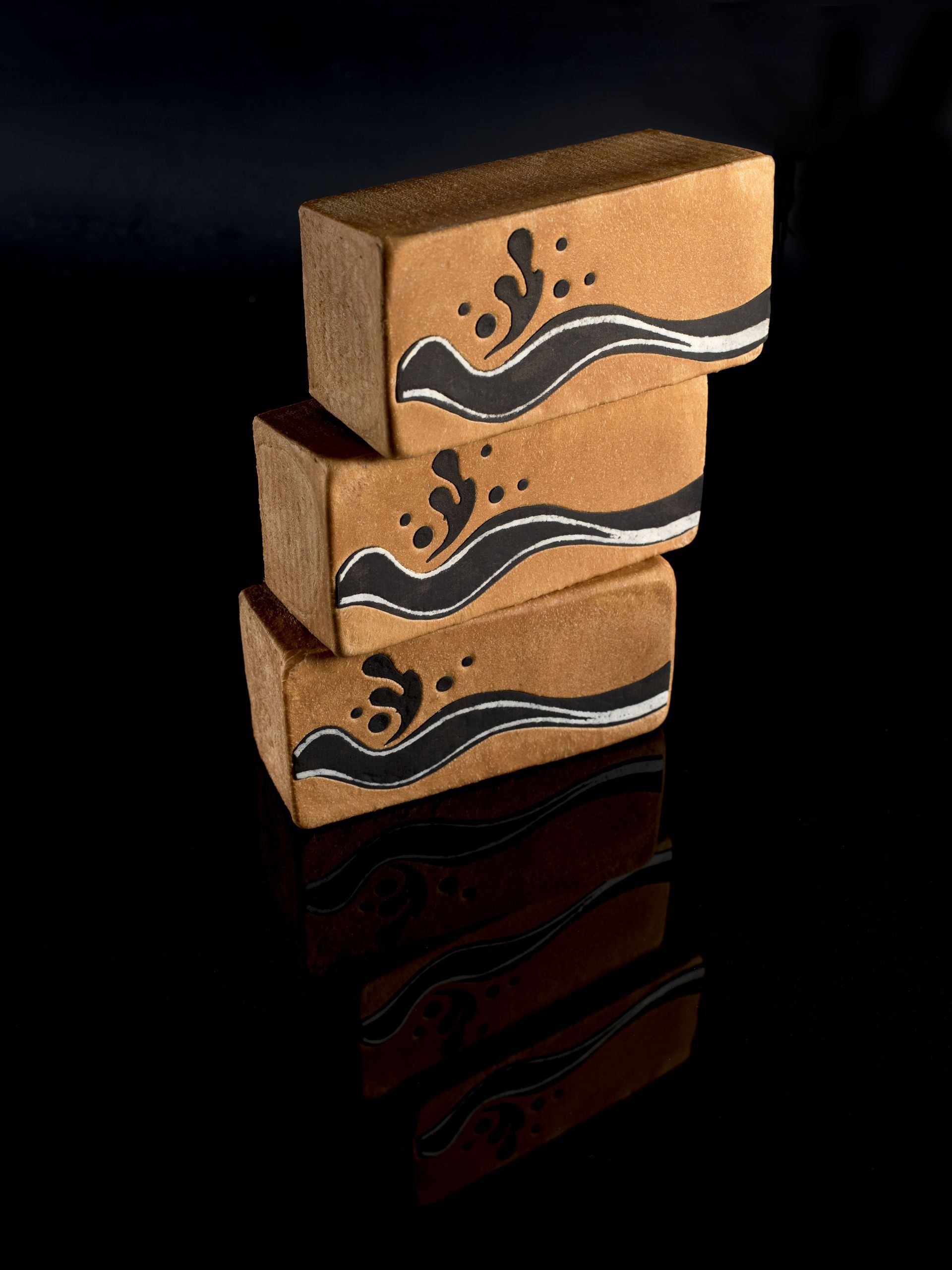 Trois briques avec des vagues dessus sont empilées les unes sur les autres sur une surface noire.