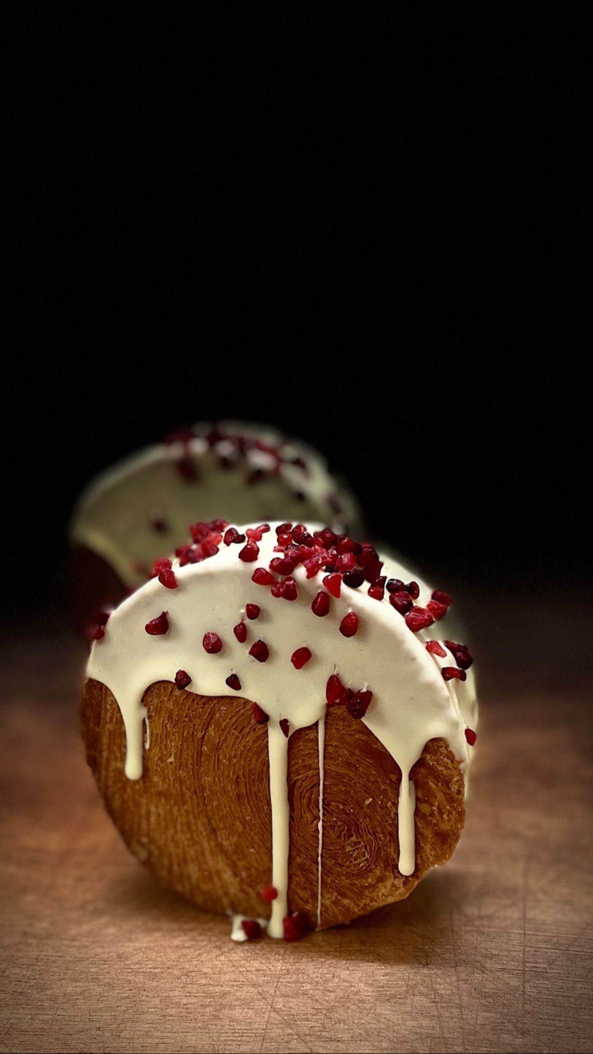 Deux beignets avec glaçage blanc et vermicelles rouges sur une table en bois.