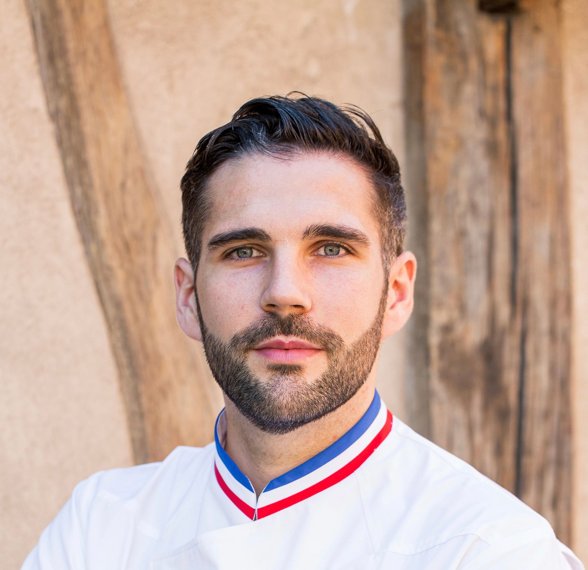Un homme avec une barbe porte une chemise blanche avec un col rouge, blanc et bleu