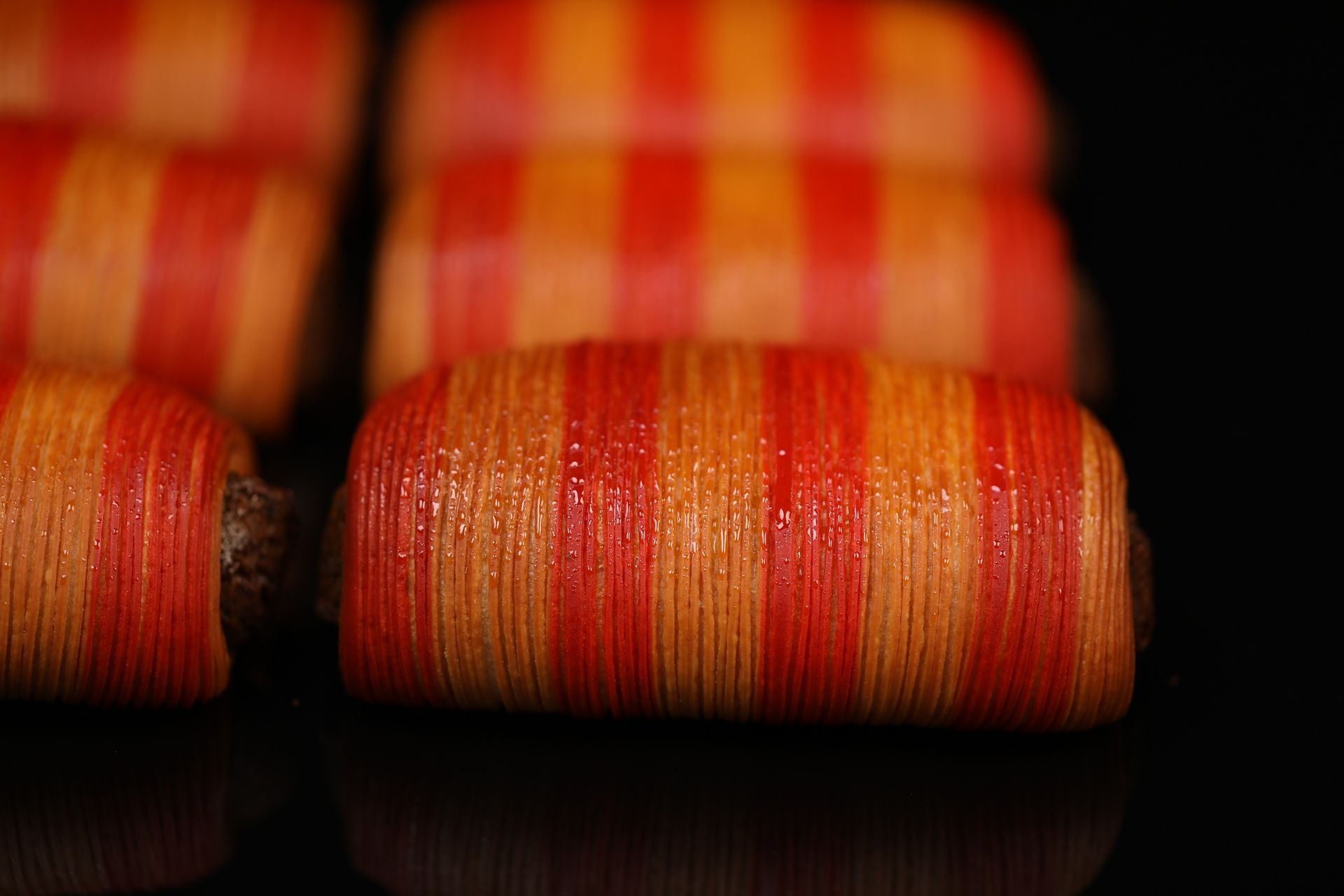 Un gros plan d'un tas de perles rayées rouges et oranges sur une surface noire.