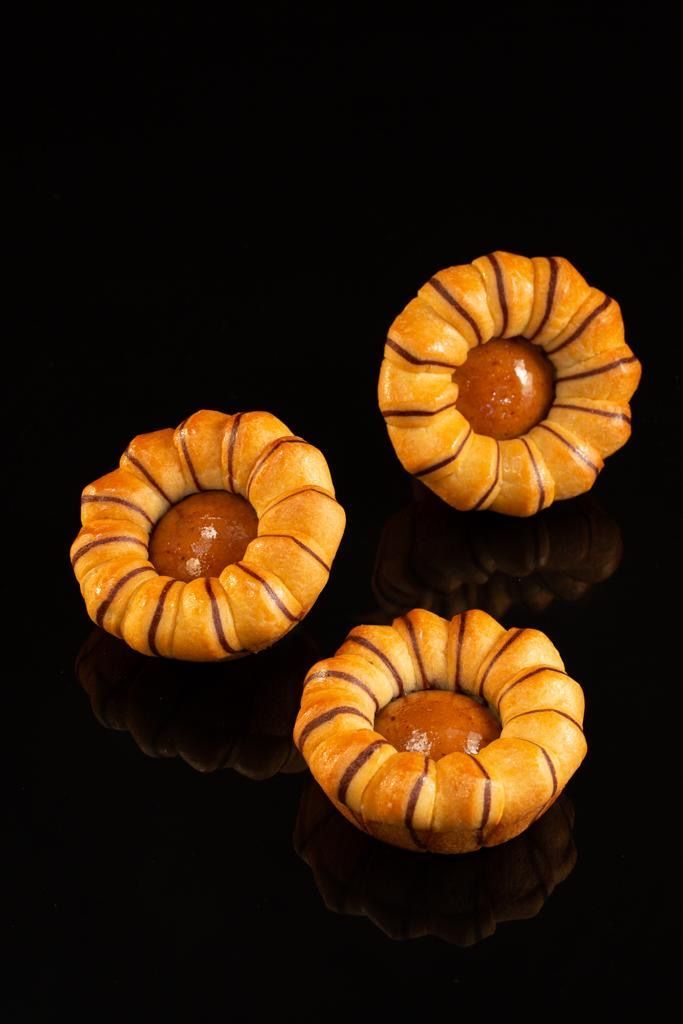 Trois biscuits en forme de fleur sont posés sur une surface noire.