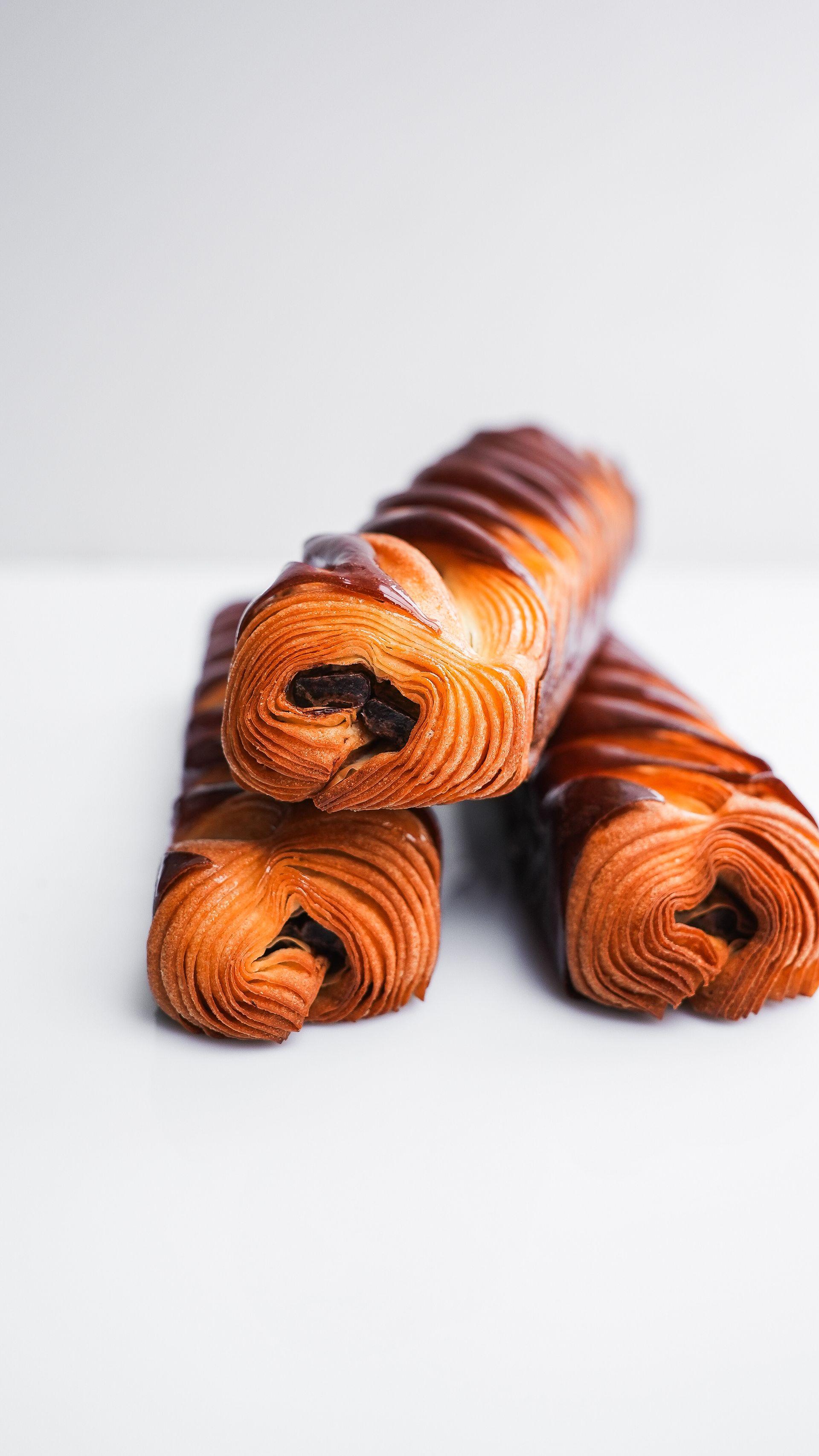 Trois croissants au chocolat sont empilés les uns sur les autres sur une surface blanche.