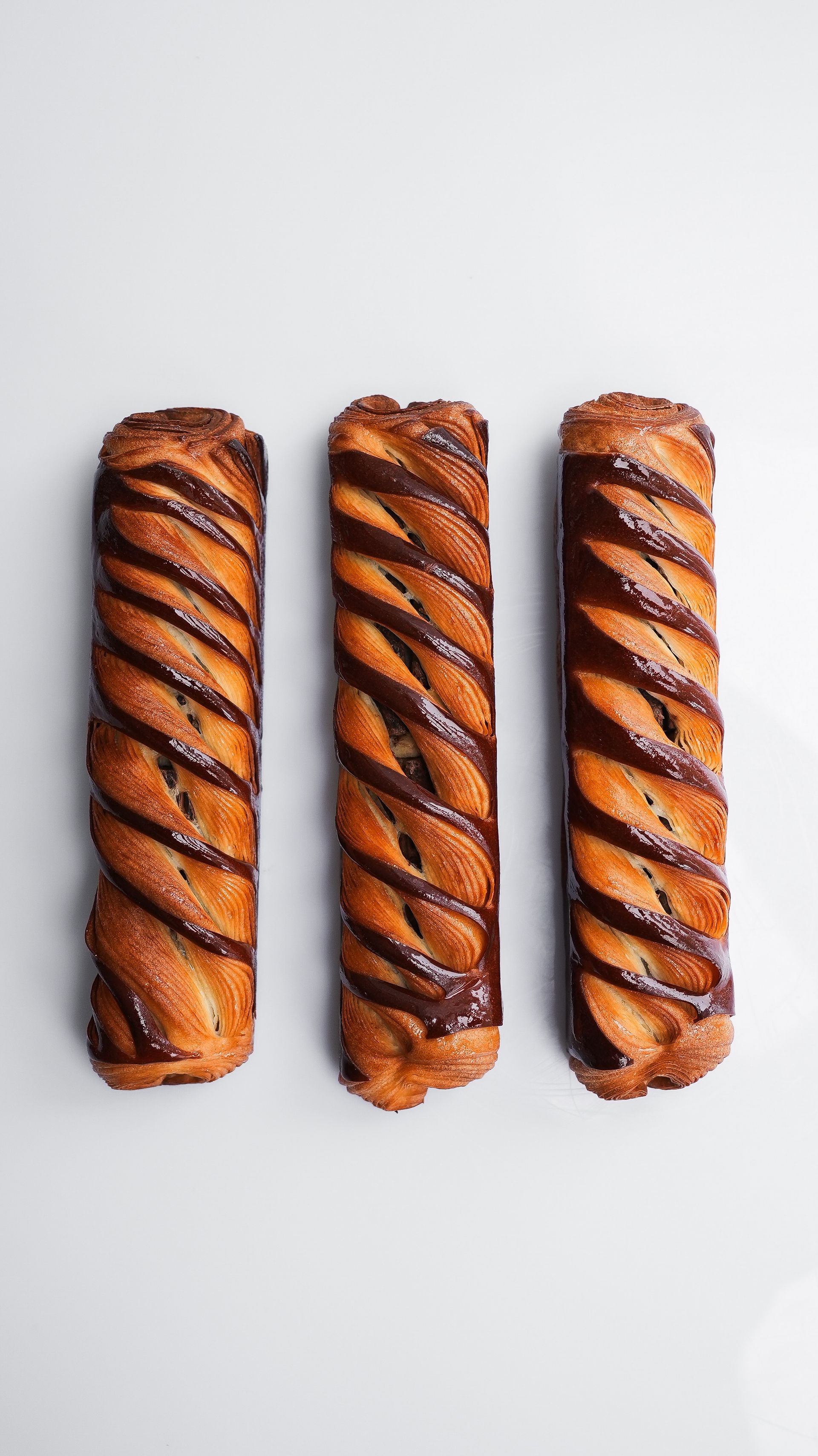 Trois bâtonnets de pâtisserie avec glaçage au chocolat sur une surface blanche.