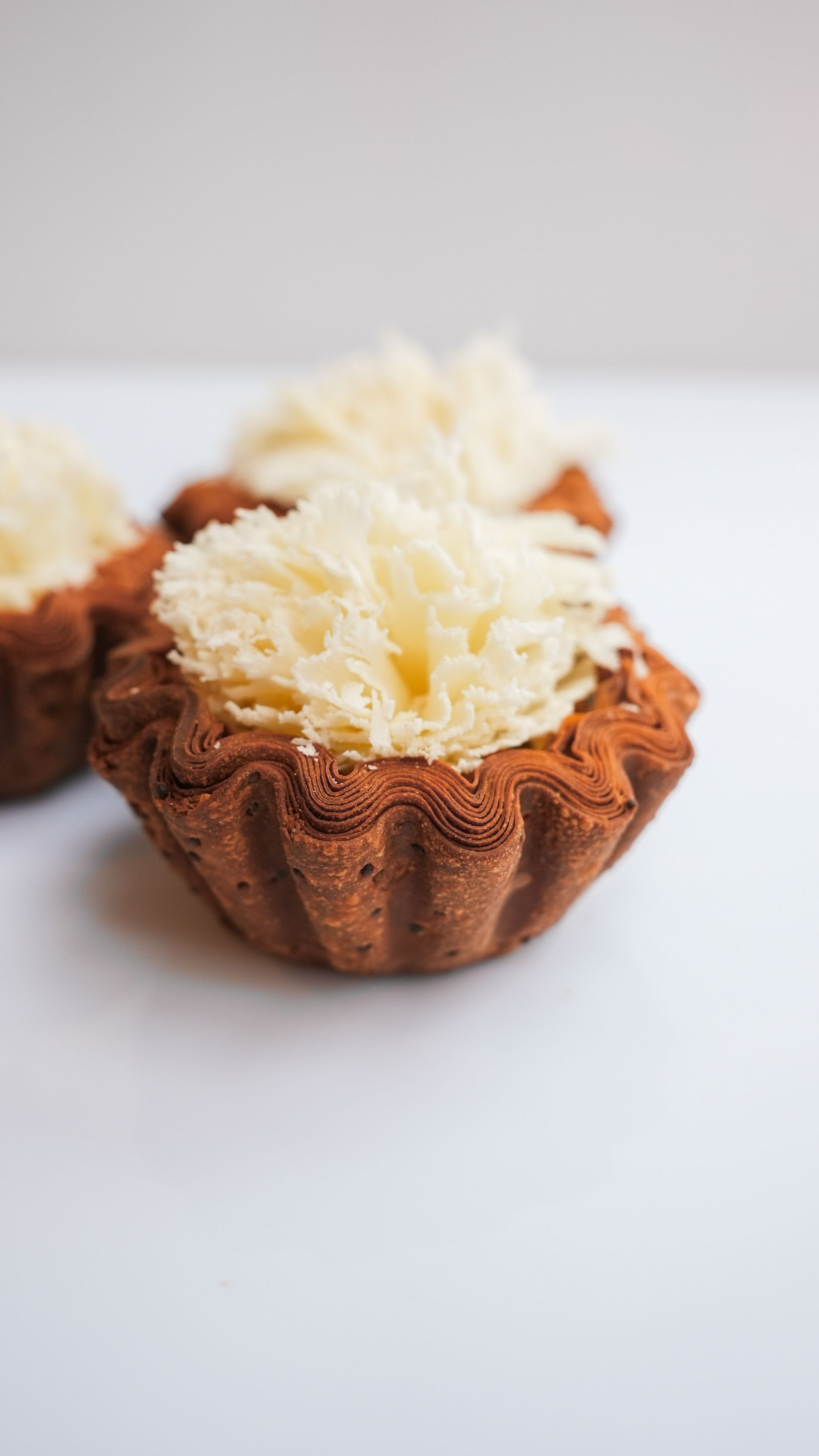 Un gros plan de trois cupcakes avec du glaçage blanc sur une surface blanche.