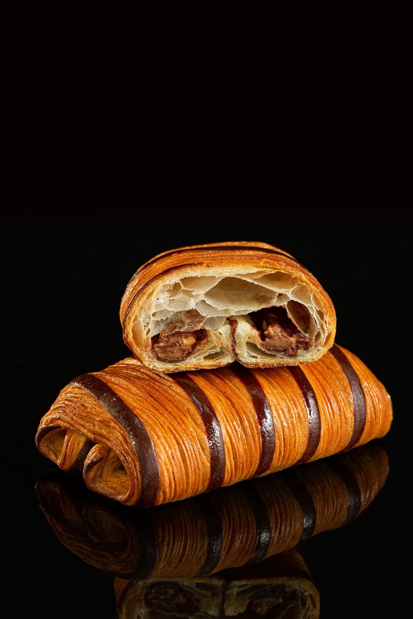 Deux croissants au chocolat sont empilés l'un sur l'autre sur une surface noire.