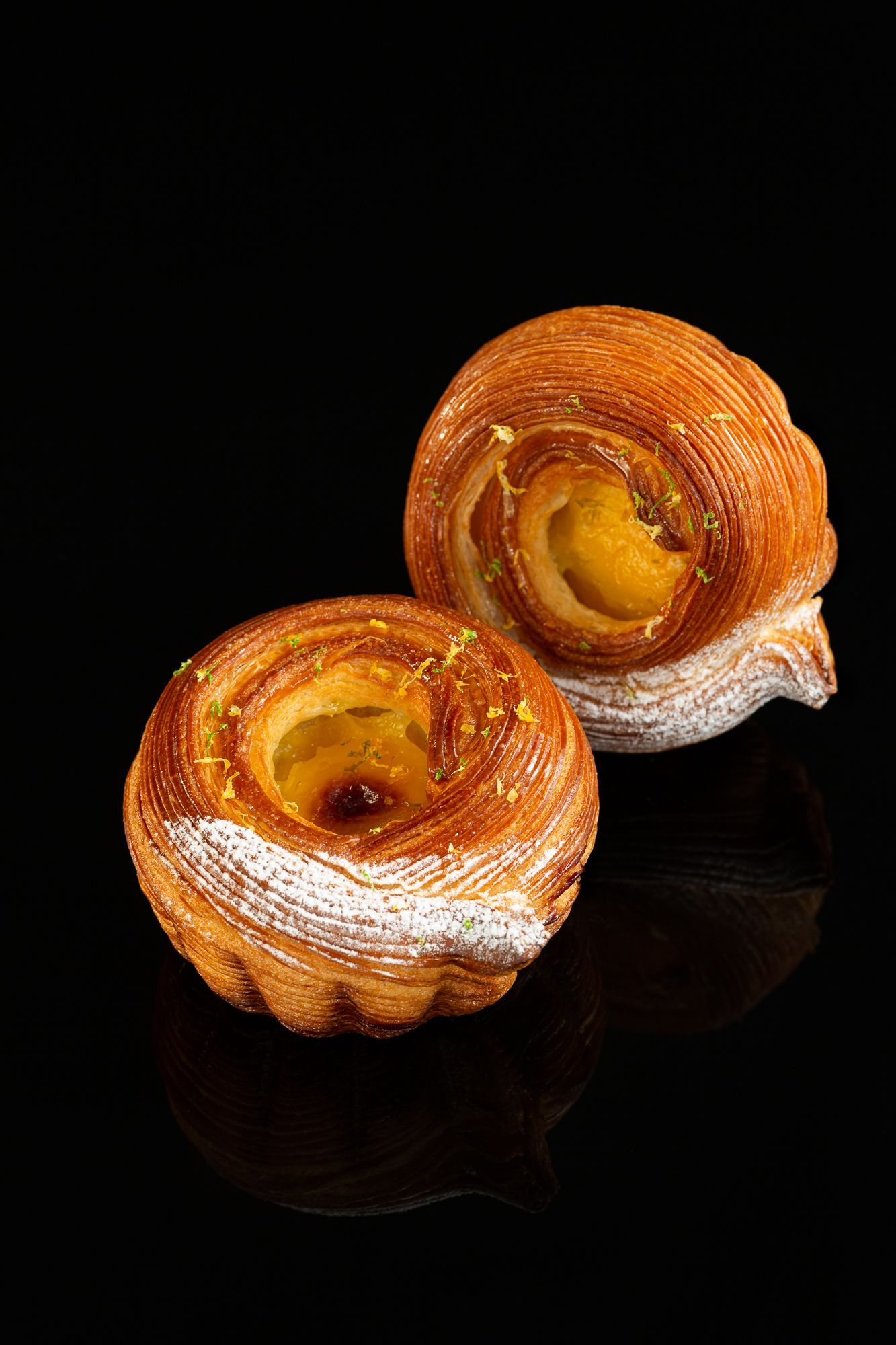 Deux pâtisseries au sucre glace sur fond noir.