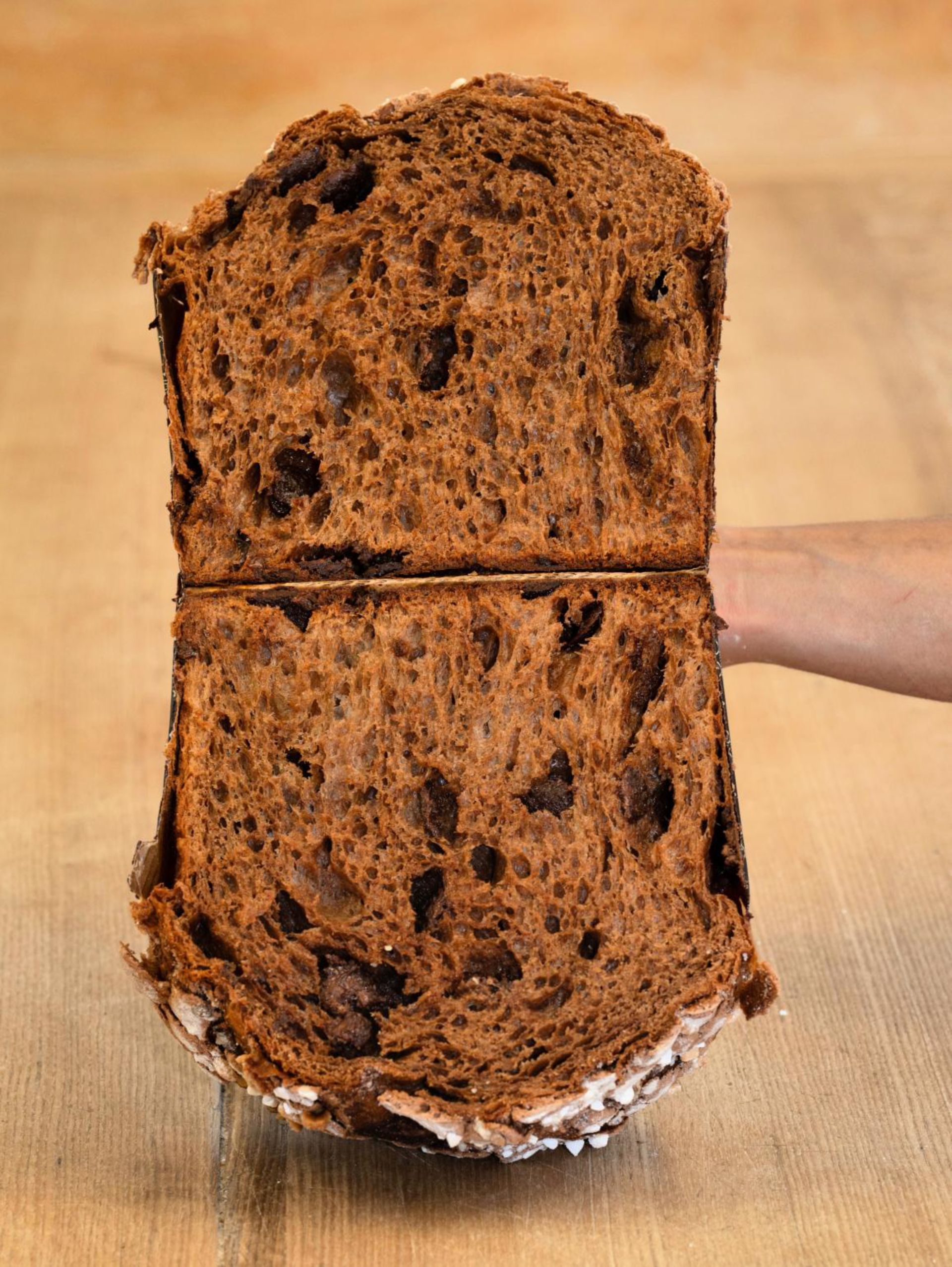 Une personne tient un morceau de pain au chocolat sur une table en bois.