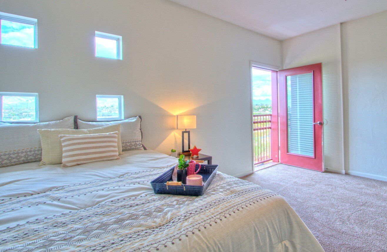 A fully furnished bedroom at The Seasons with private balcony, plush carpeting, and stylish decor with a bed tray.