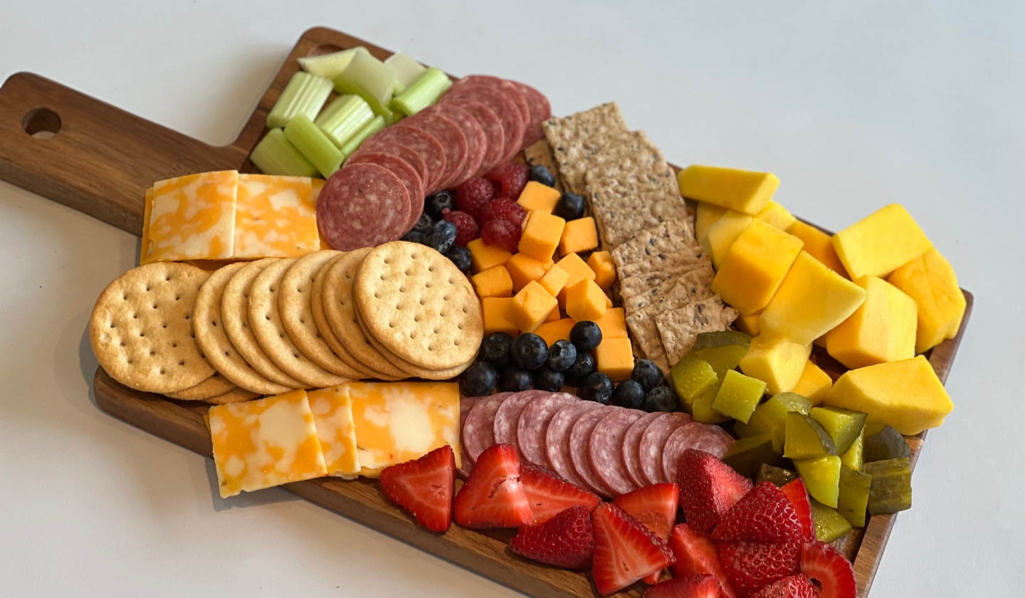 A charcuterie board with crackers, salami, cheese, and fruit.