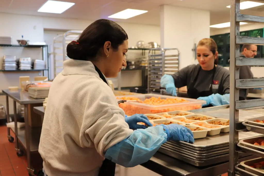 Three volunteers in hairnets and gloves prepare meals in Tucson at the Community Food Bank of Southern AZ.