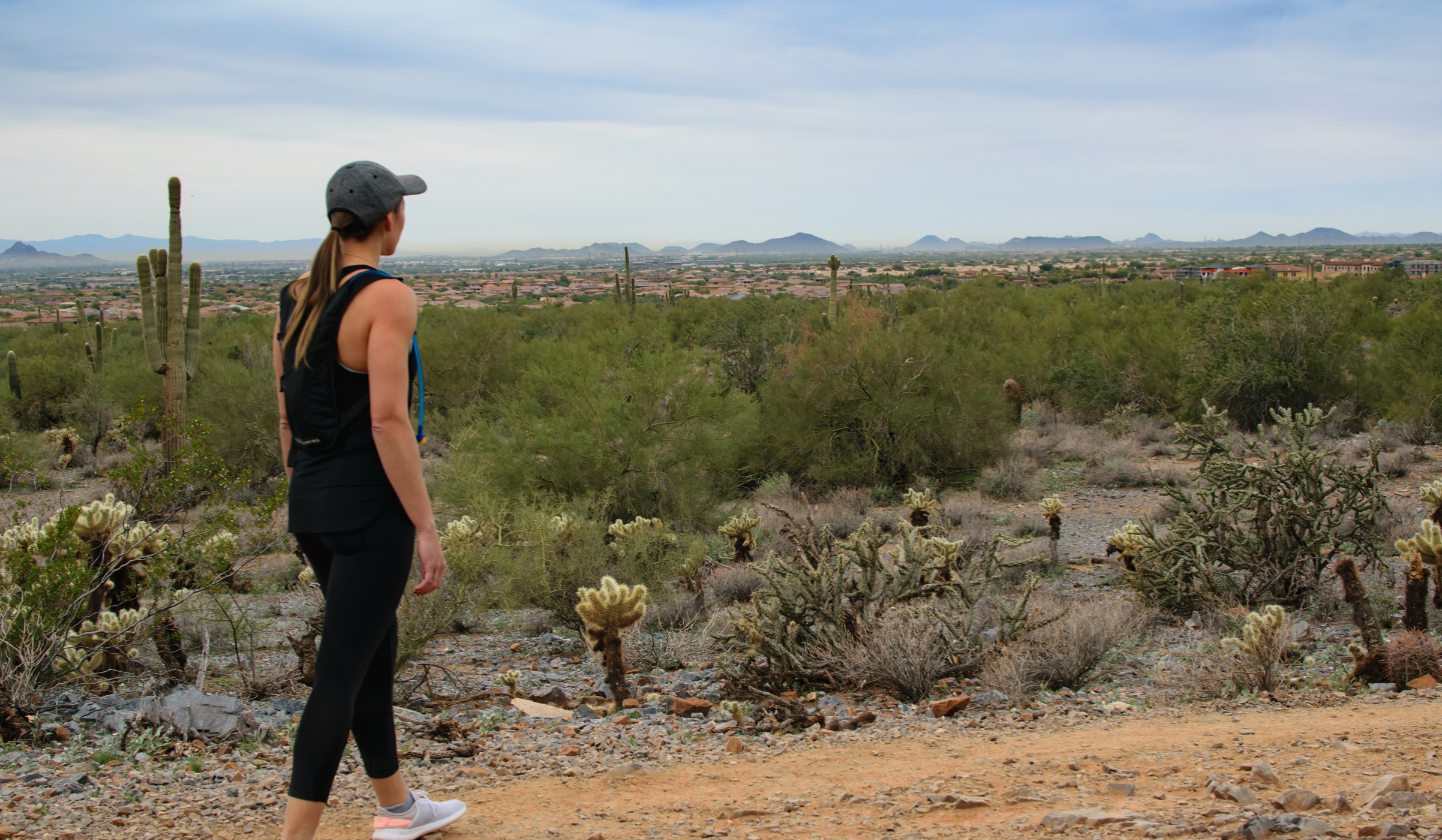 Layer on sun screen! Female hiker in the Arizona desert wearing a hat, loose-fitting clothing that covers skin, and sneakers.