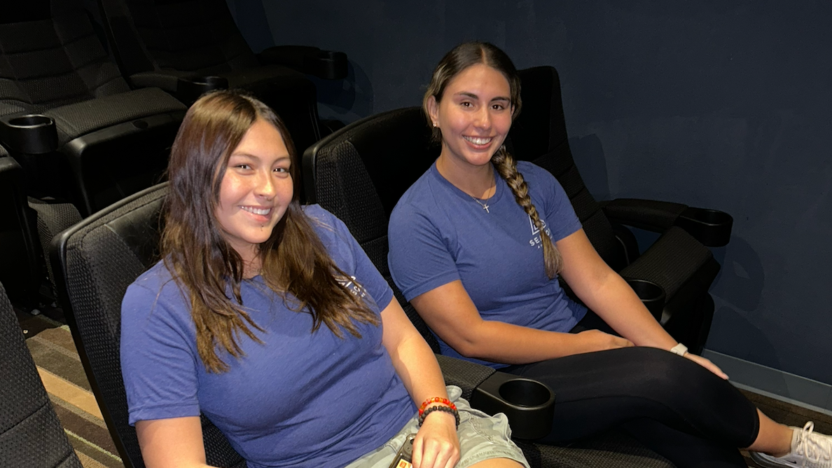 Two female residents sitting in the recliner seats of the on-site movie theater.