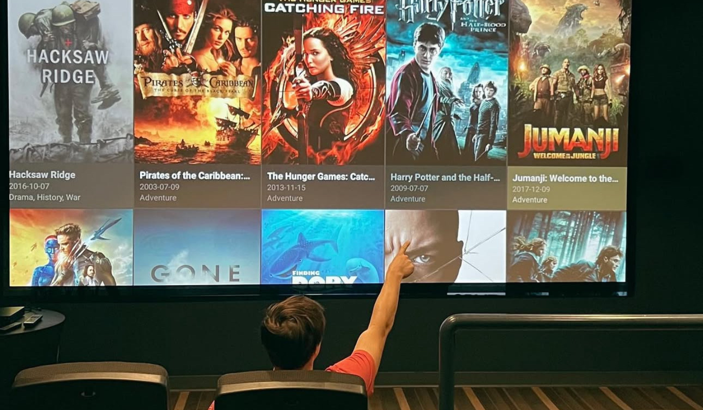 Male resident picking which movie to stream at The Seasons' on-site movie theater with lounge chairs and a big screen.