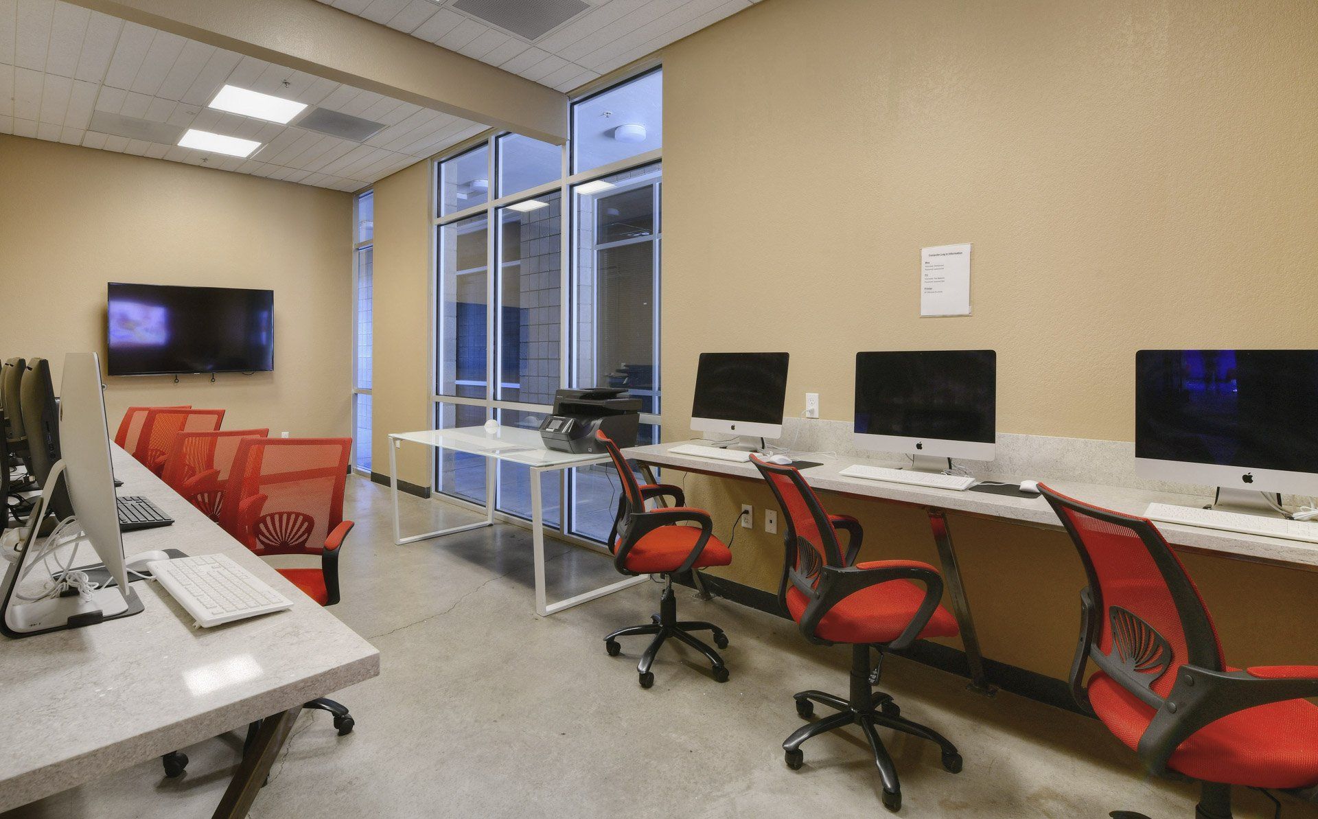 A view of The Seasons' Computer lab with iMacs, Dells, and red office chairs. 
