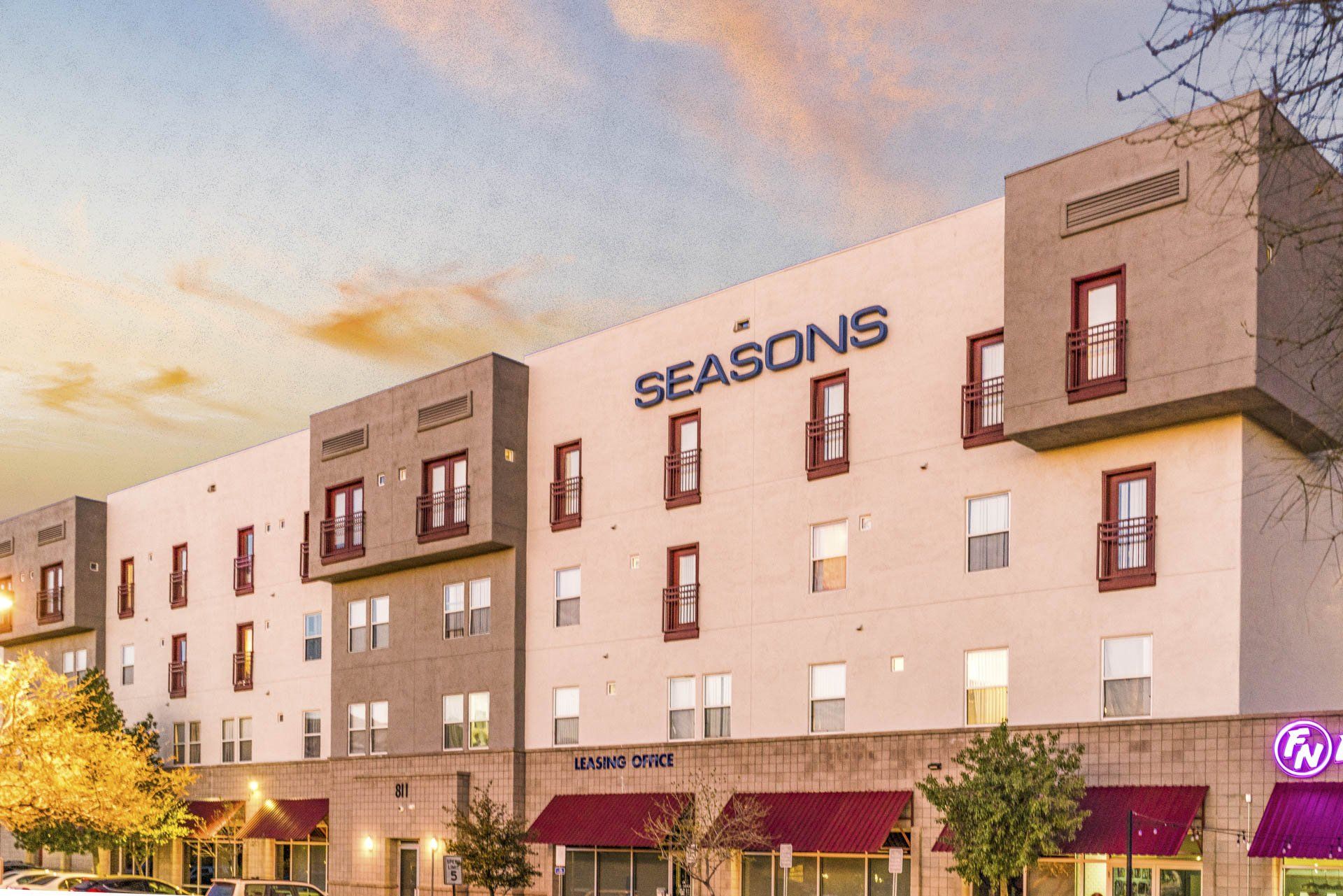 The front of The Seasons student living complex with a pink and blue sky.