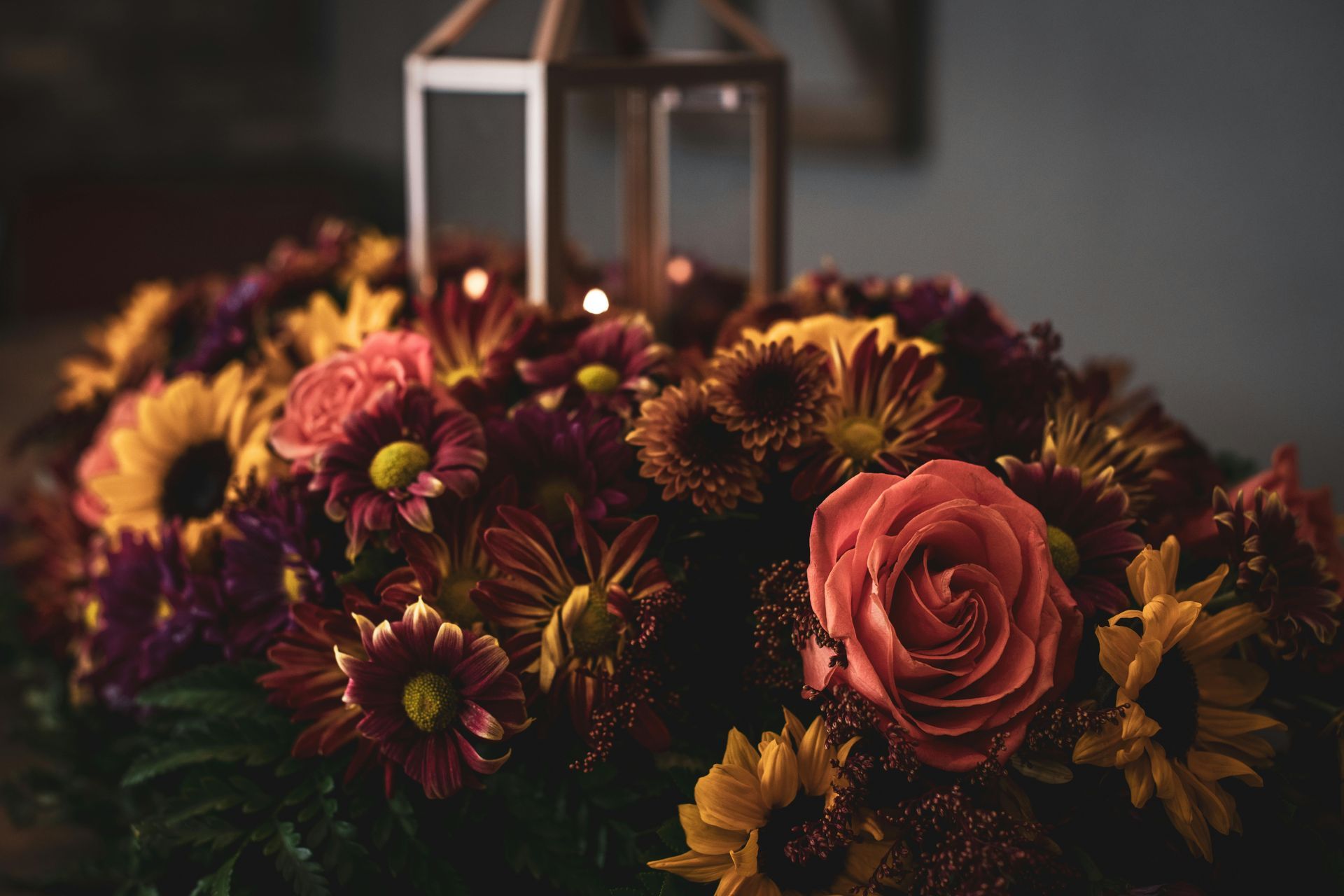 A mix of sunflowers, roses, daisies, and carnations with a rustic candle holder.