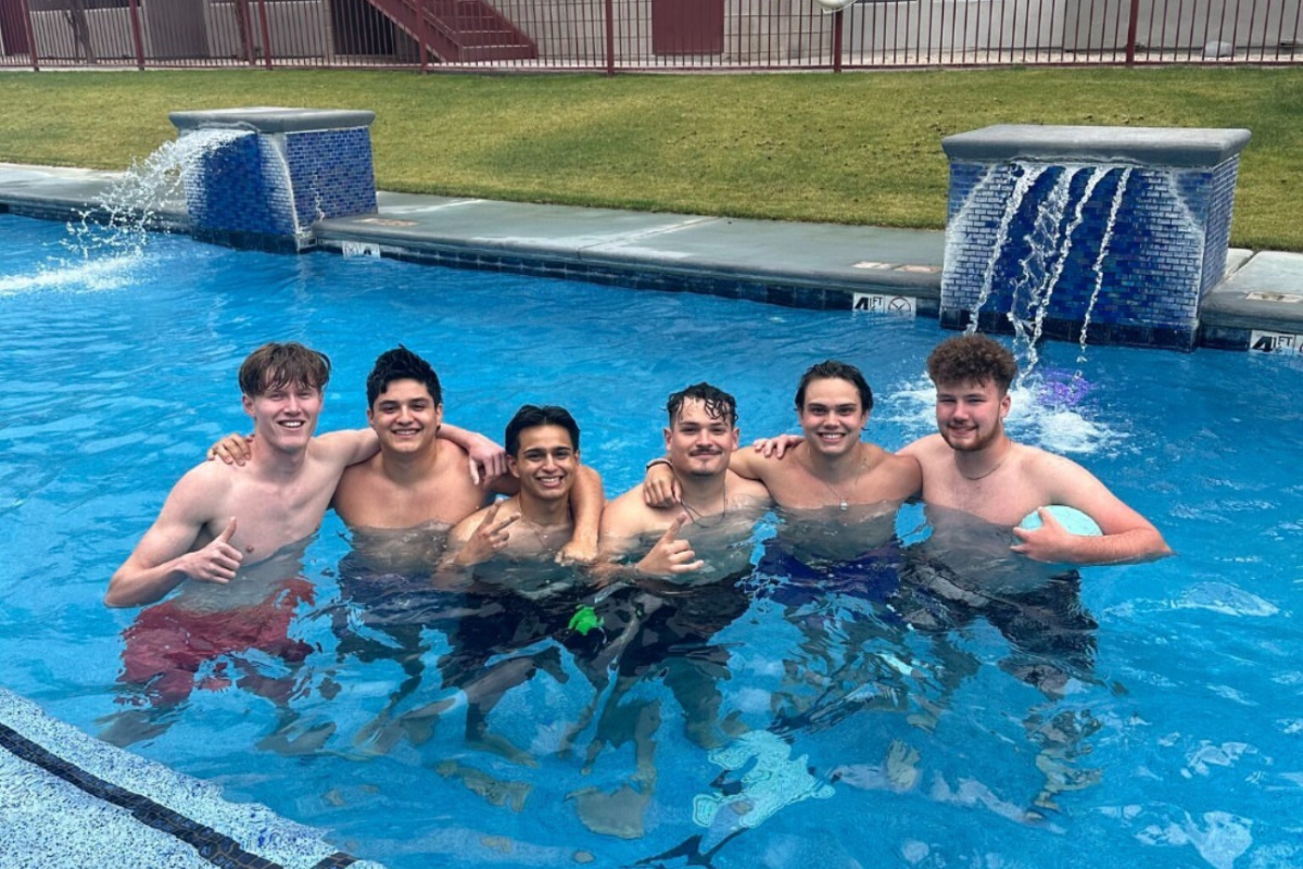 Six male residents stand in the pool, arms around each other, smiling at the camera.