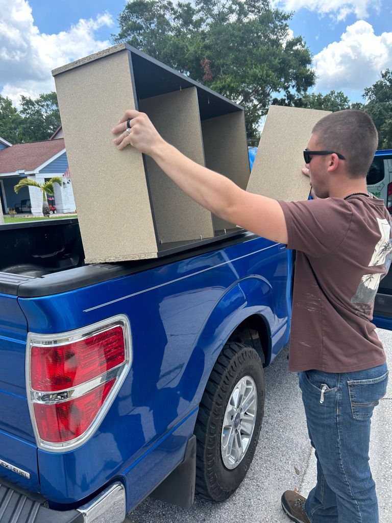 Man loading a three-compartment shelf into the bed of a blue pickup truck on a sunny day.