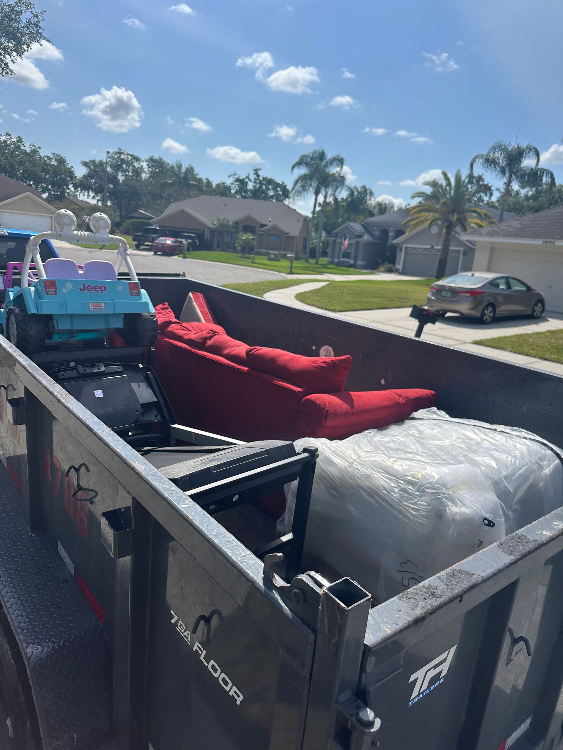 A red sofa and other items fill a black trailer parked in a residential neighborhood on a sunny day.