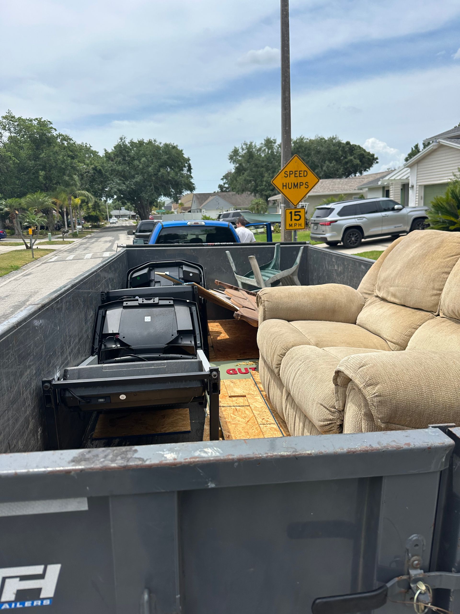 Dumpster filled with furniture and debris on a residential street; a beige recliner sofa is visible.