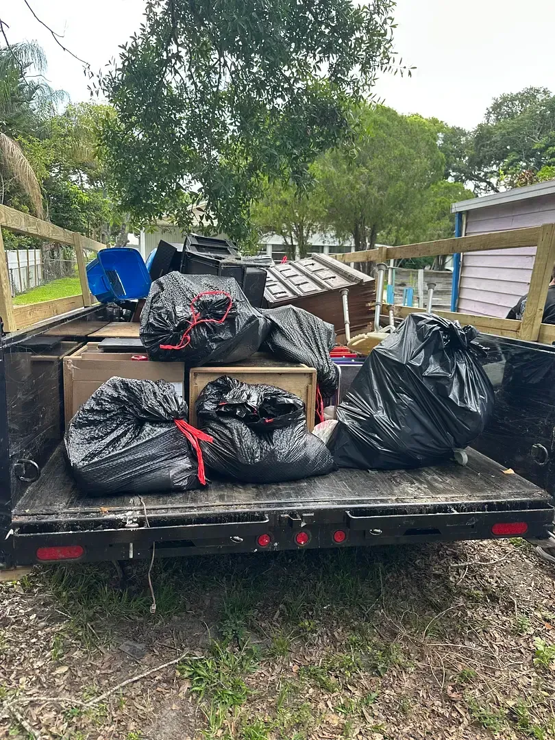 A trailer loaded with black trash bags, cardboard boxes, and other items, likely for disposal; outdoors.