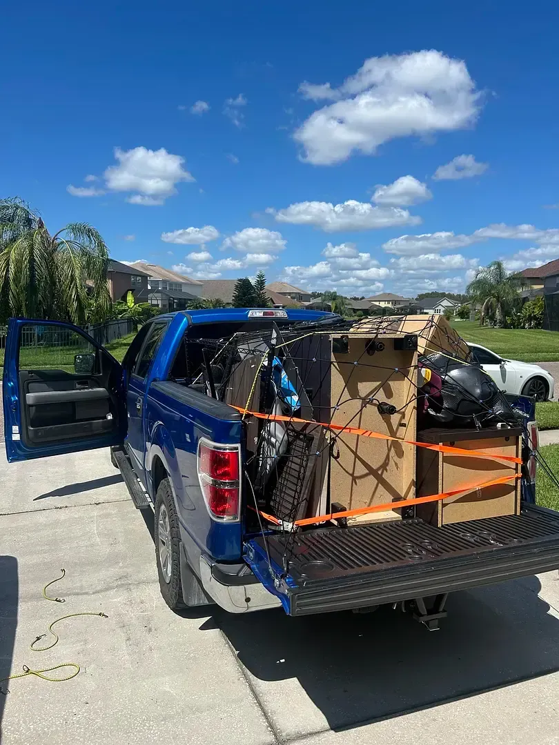 Blue pickup truck loaded with furniture and boxes on a sunny day. The truck bed is open.