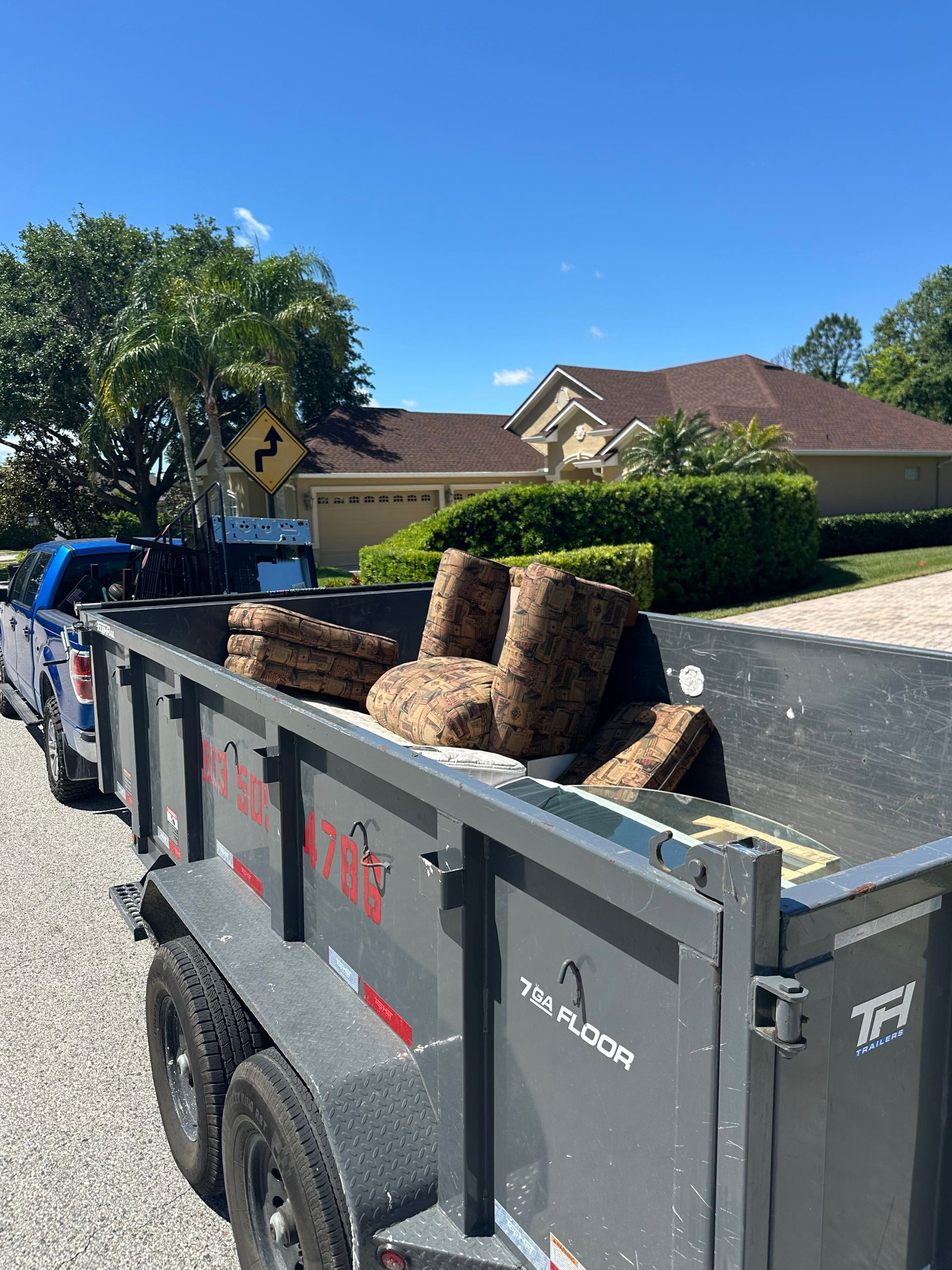 A trailer loaded with discarded furniture in front of a house on a sunny day.
