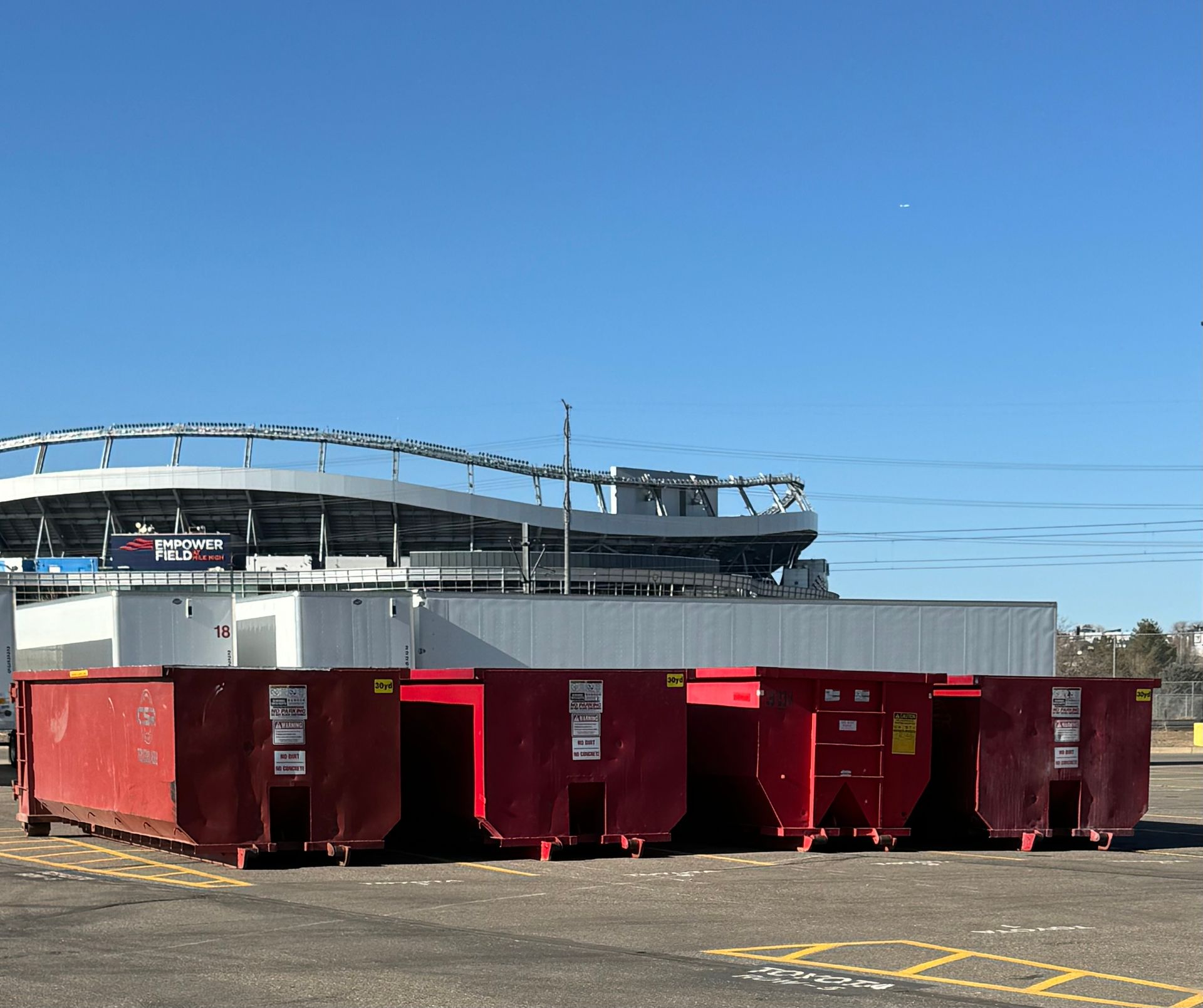 Red dumpsters in front of a stadium on a sunny day.