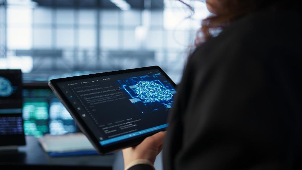 Person holding a tablet displaying a blue data map and code; indoor setting.