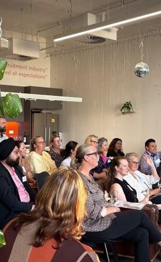 A group of people sitting in chairs during an indoor presentation or workshop, with one person raising their hand.