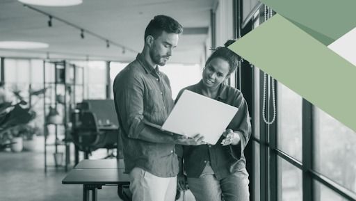 People working at desks in an office; one with headphones, and computers. Windows in the background.