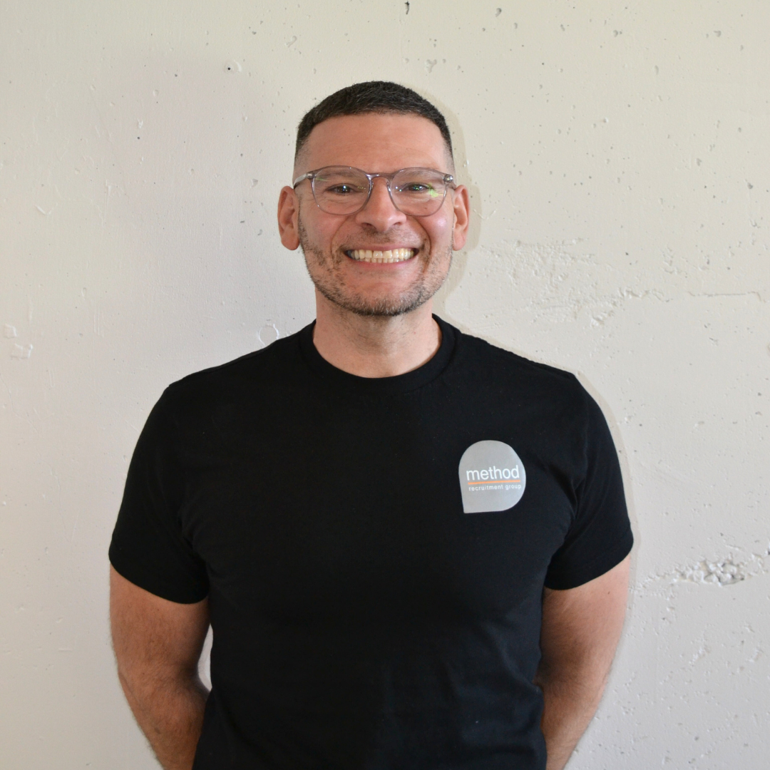 Three men in black hoodies smiling, posing in front of an orange wall with the 