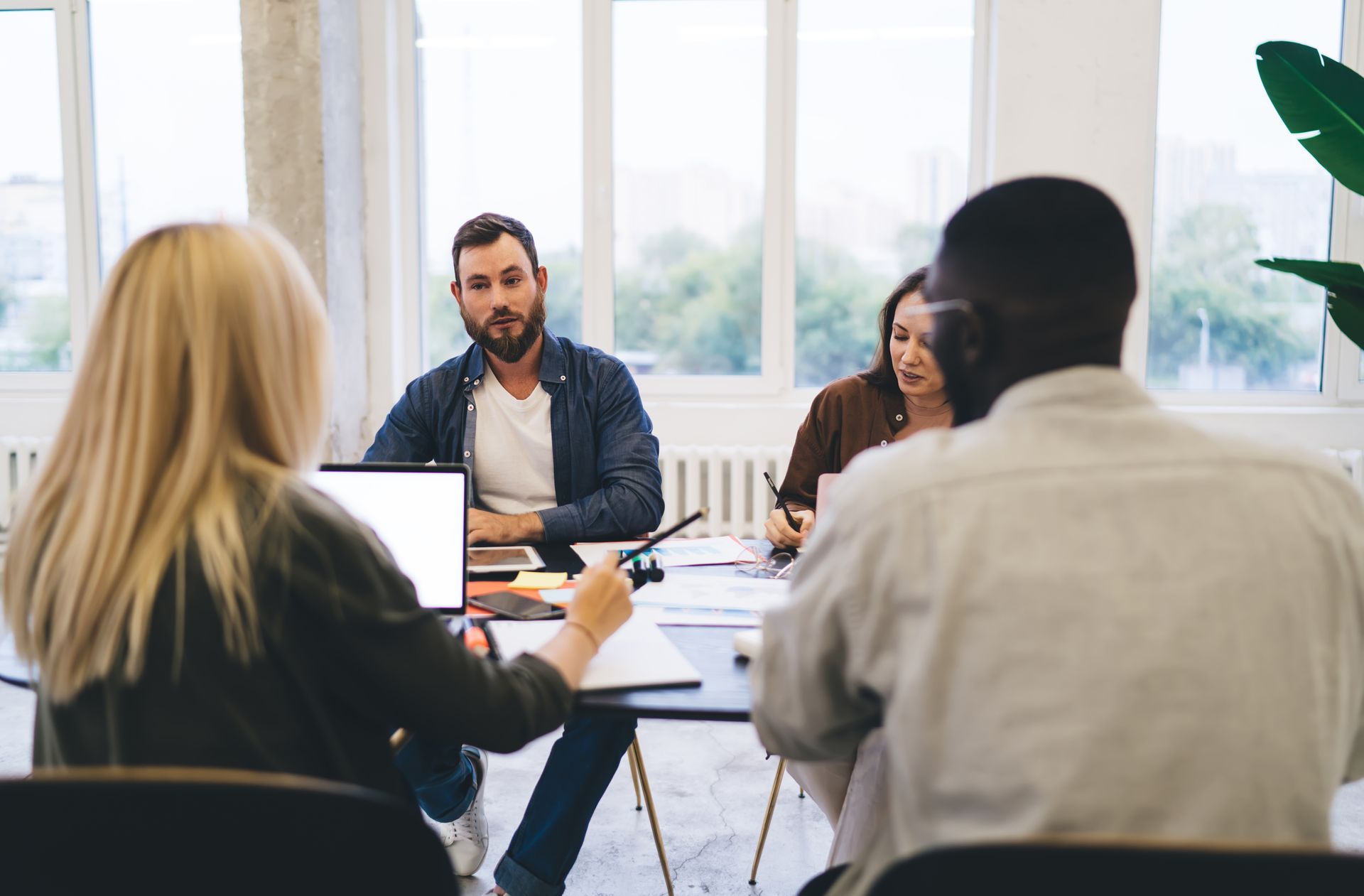 Man shaking hands with another person at a table, near a laptop and coffee cups.