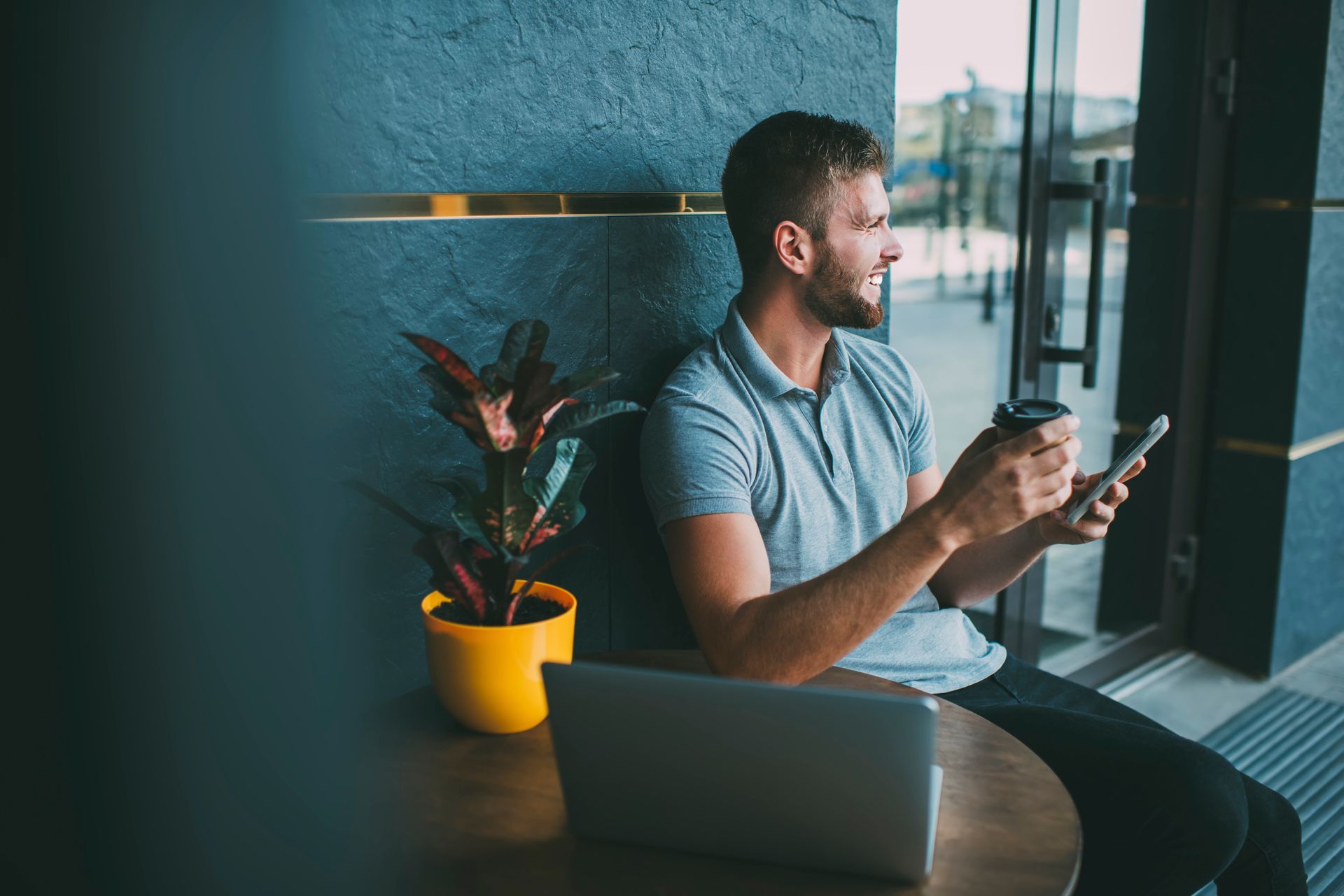 Man shaking hands with another person at a table, near a laptop and coffee cups.