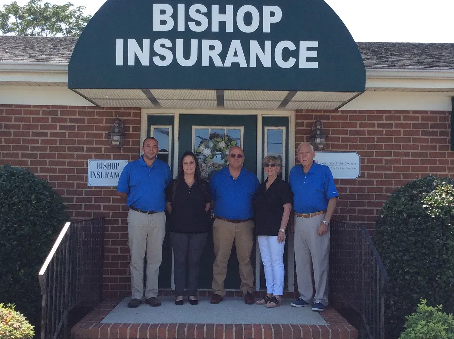 Five people in front of Bishop Insurance, a brick building with a green awning. They all wear blue or black shirts.