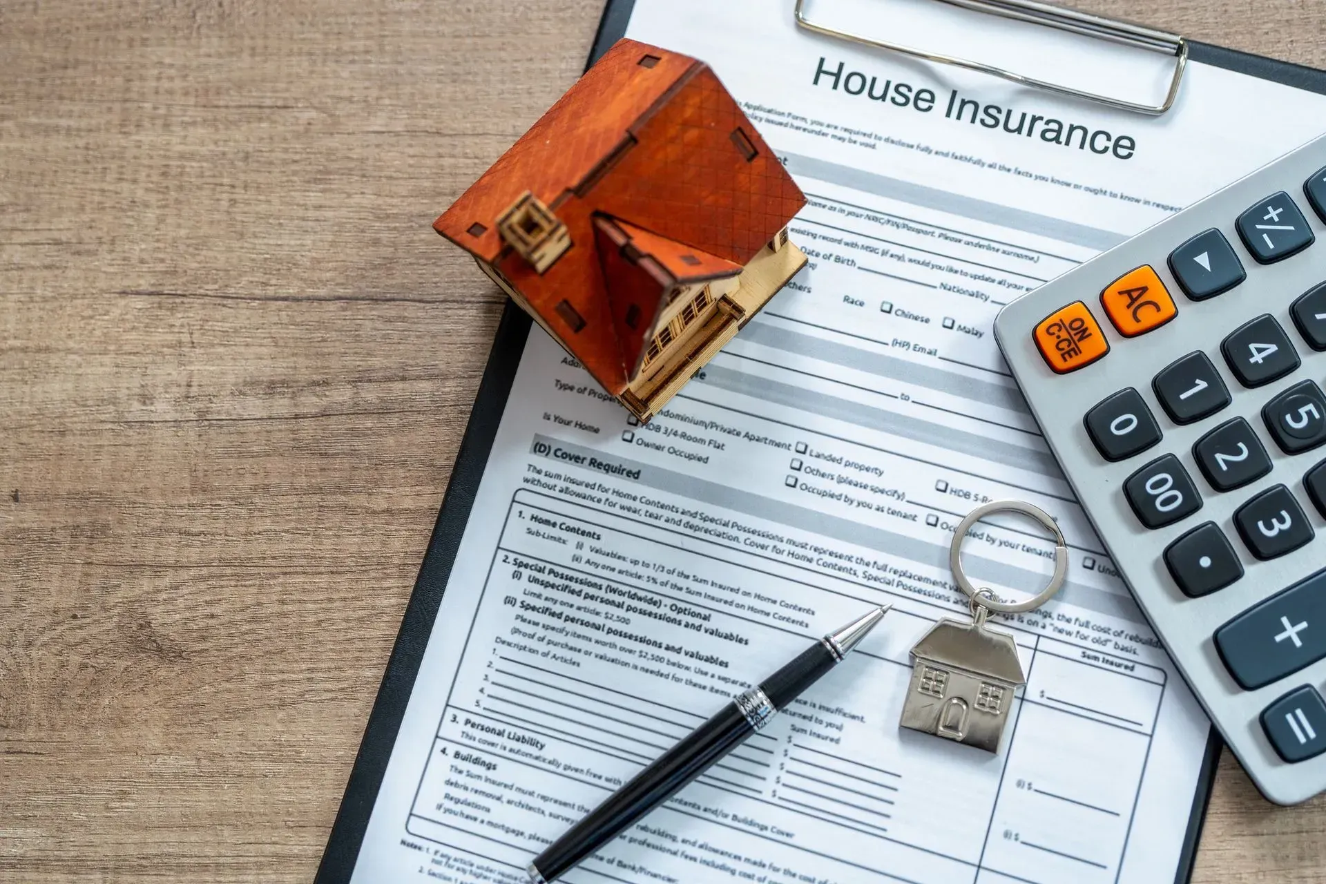 House insurance paperwork with a toy house, calculator, pen, and house key on a wooden table.