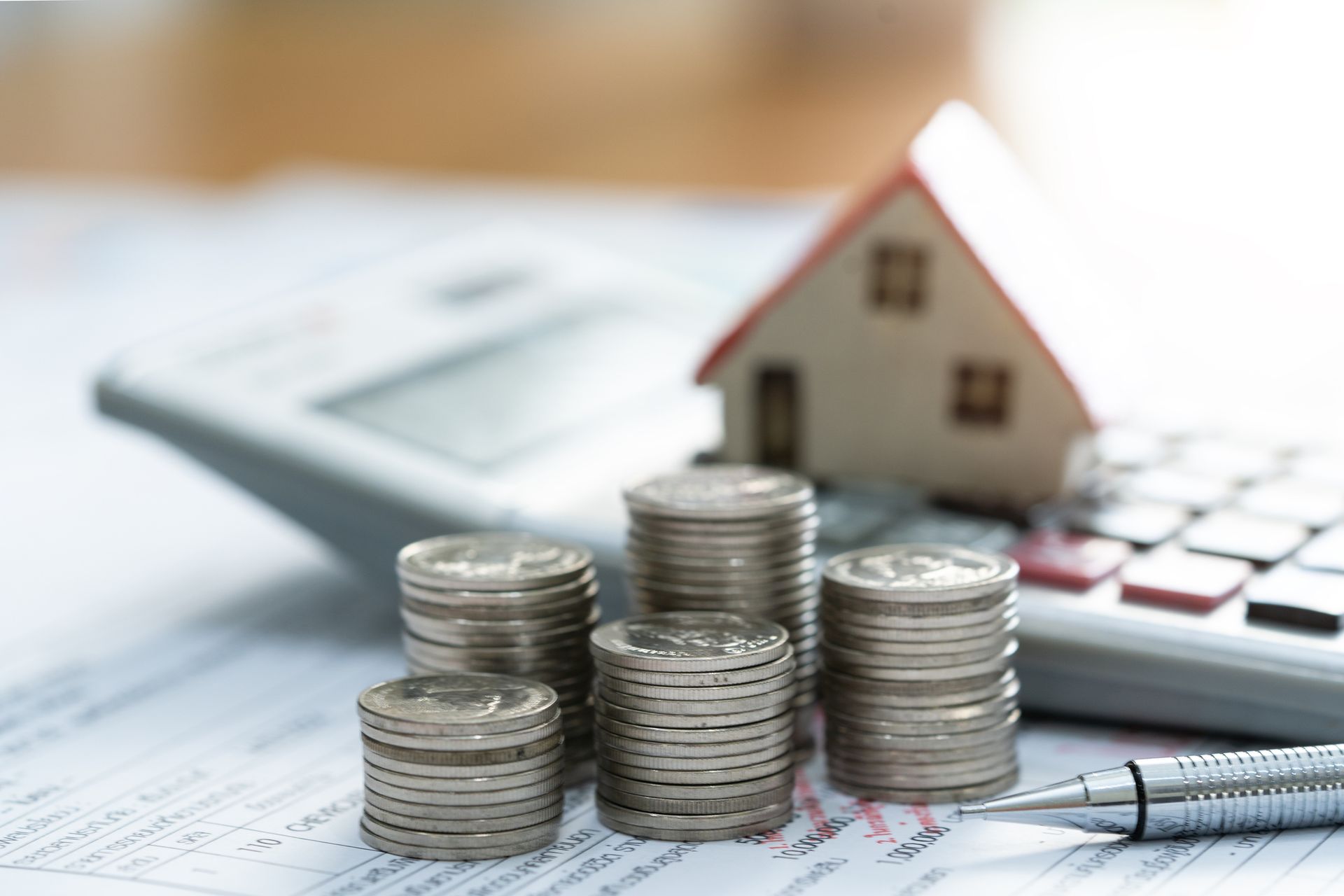 Stacks of coins, a toy house, calculator, and pen on a financial document, illustrating real estate budgeting and savings.