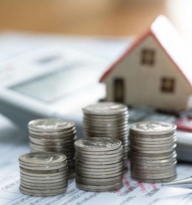 Stacks of coins, a toy house, calculator, and pen on a financial document, illustrating real estate budgeting and savings.