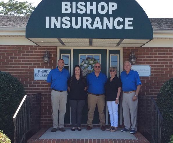 Five people in front of Bishop Insurance, a brick building with a green awning. They all wear blue or black shirts.