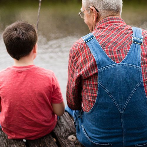 A man and a boy are sitting on a dock looking at the water.