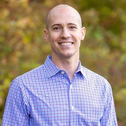 A bald man in a plaid shirt is smiling for the camera.