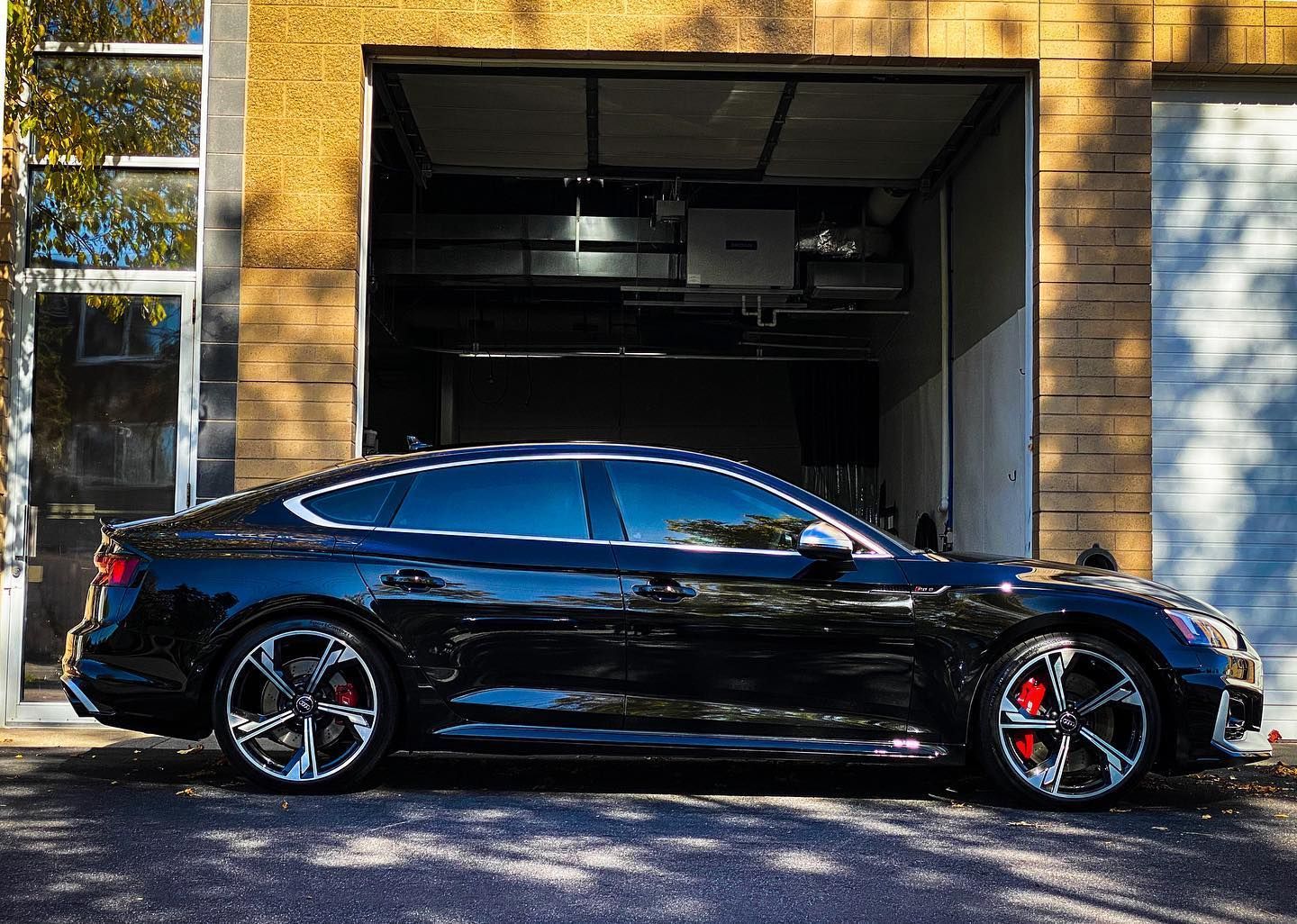 Black Audi RS5 sedan parked outside garage.