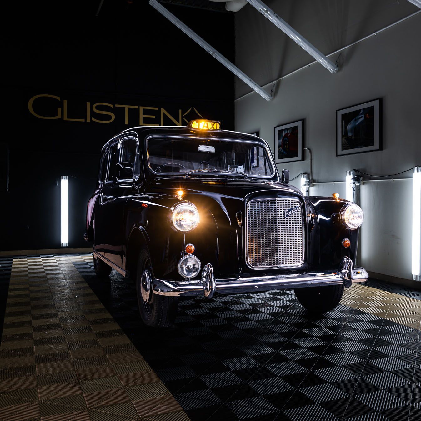 Black London taxi cab with the light on, on a checkered floor indoors.