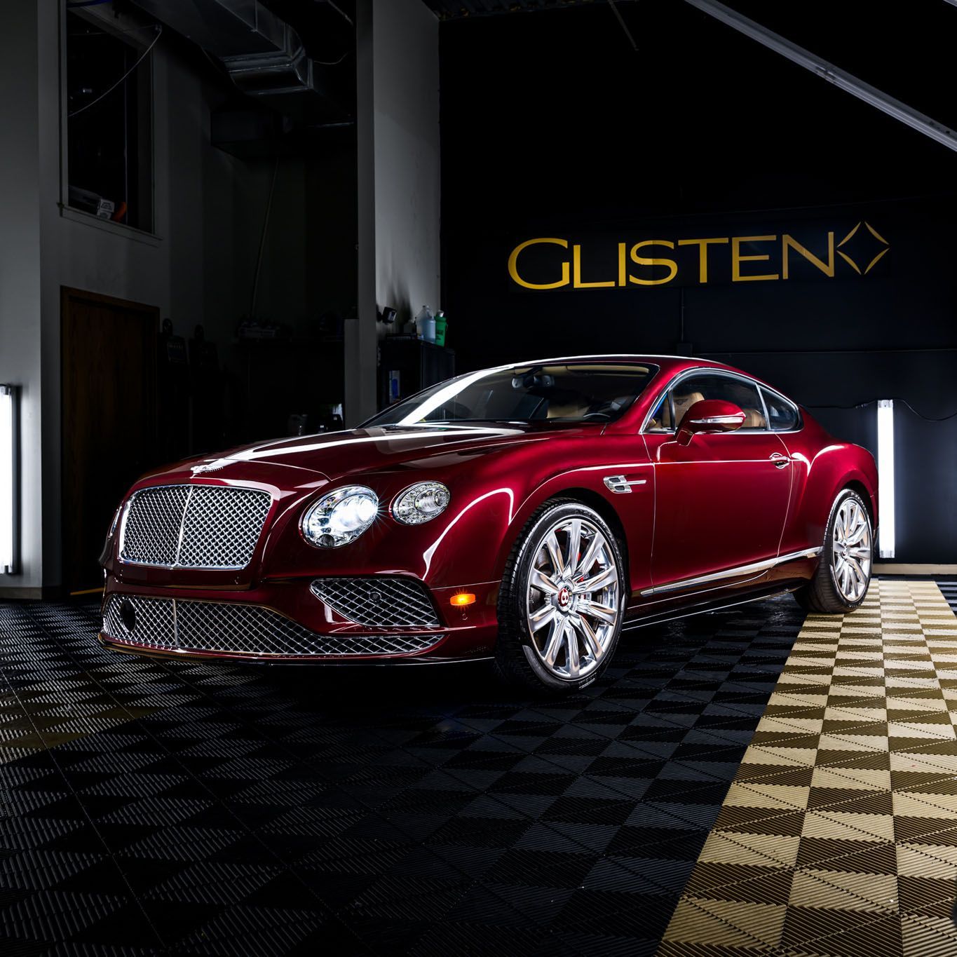 Red Bentley coupe parked in a detail shop; glossy finish.