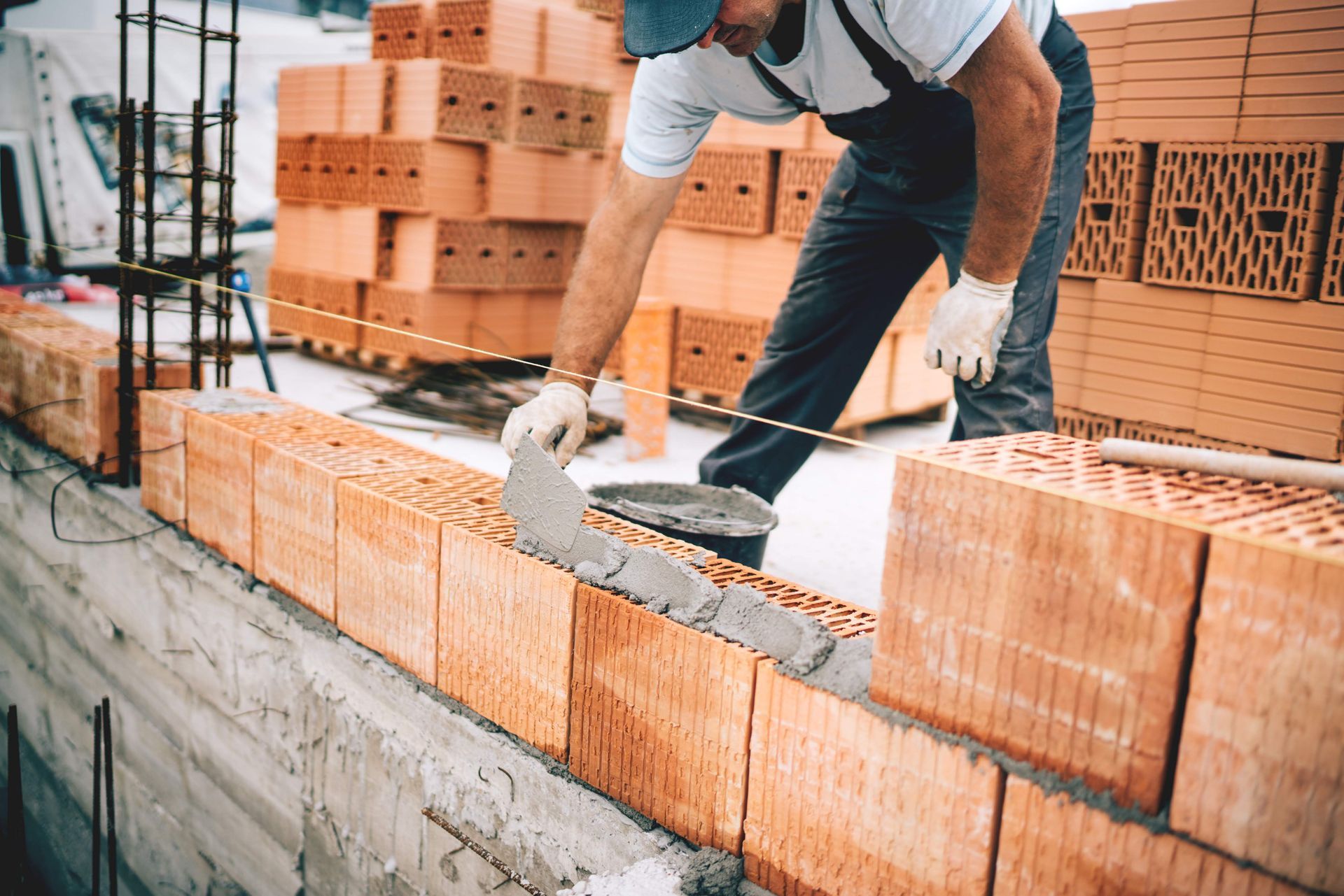 Worker using a rubber hammer and gloves to lay cement pavement on a sandy walkway.